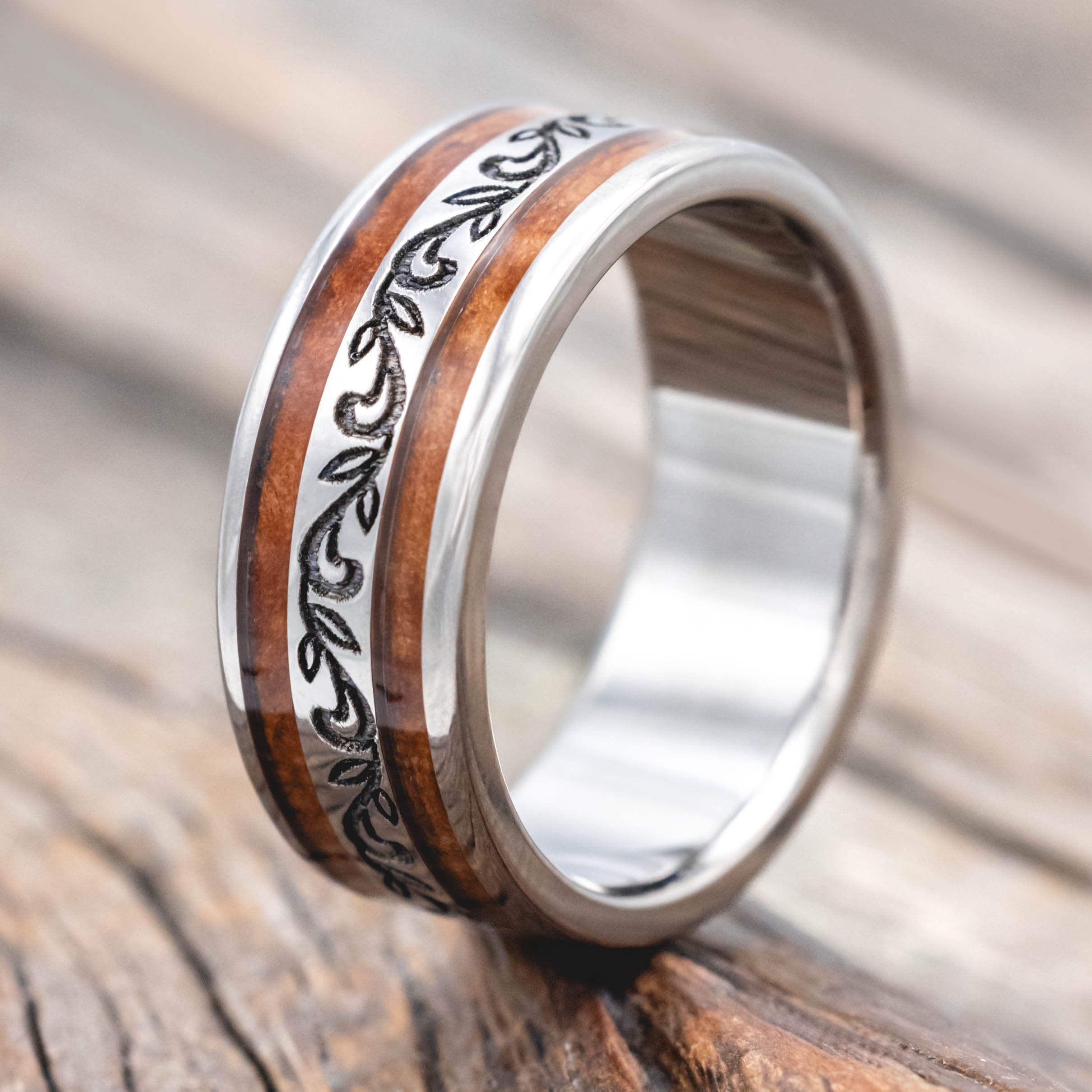 Silver ring with redwood inlay and paisley engraving on a wooden surface