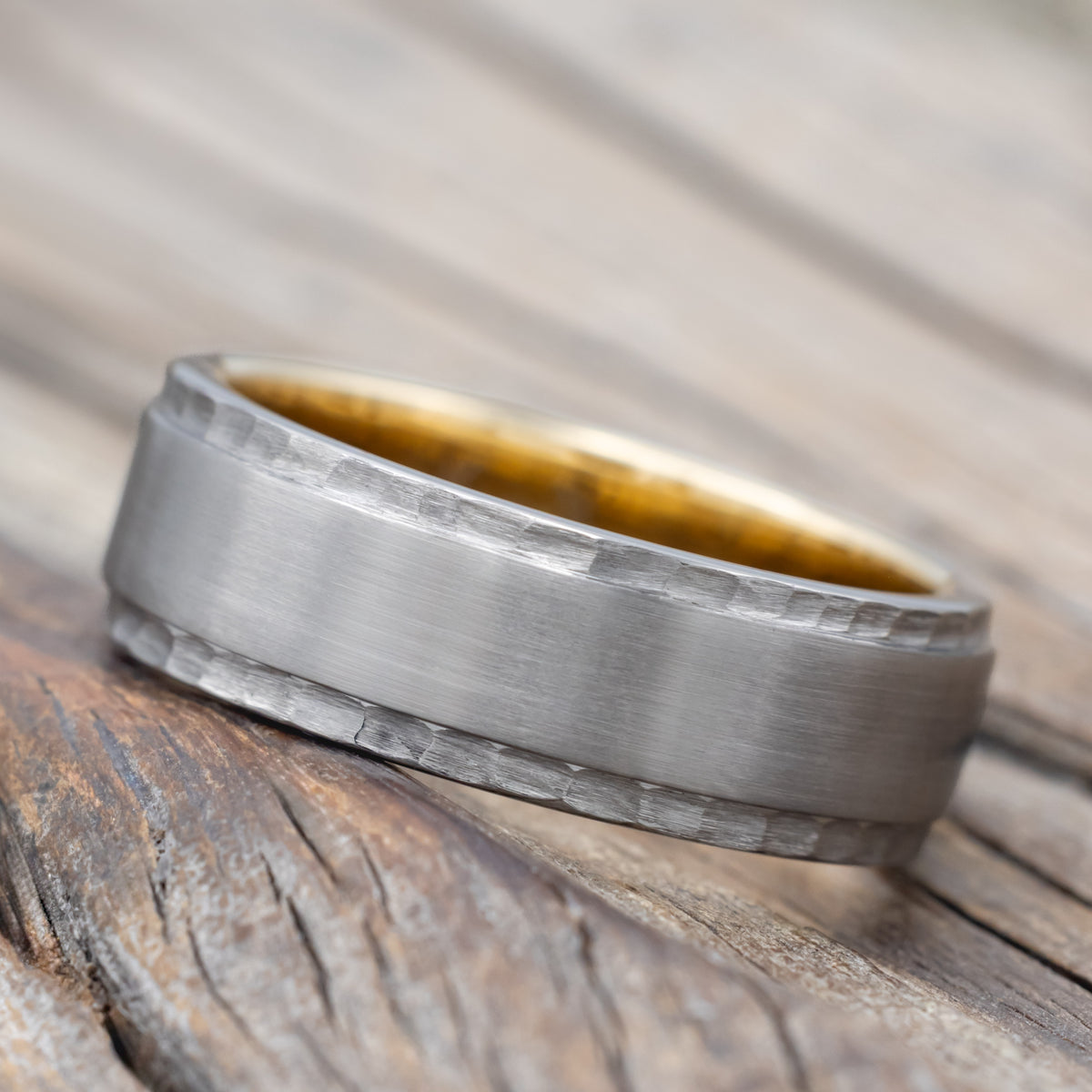 A titanium wedding ring with brushed center and hammered edges with gold lining on a wooden surface