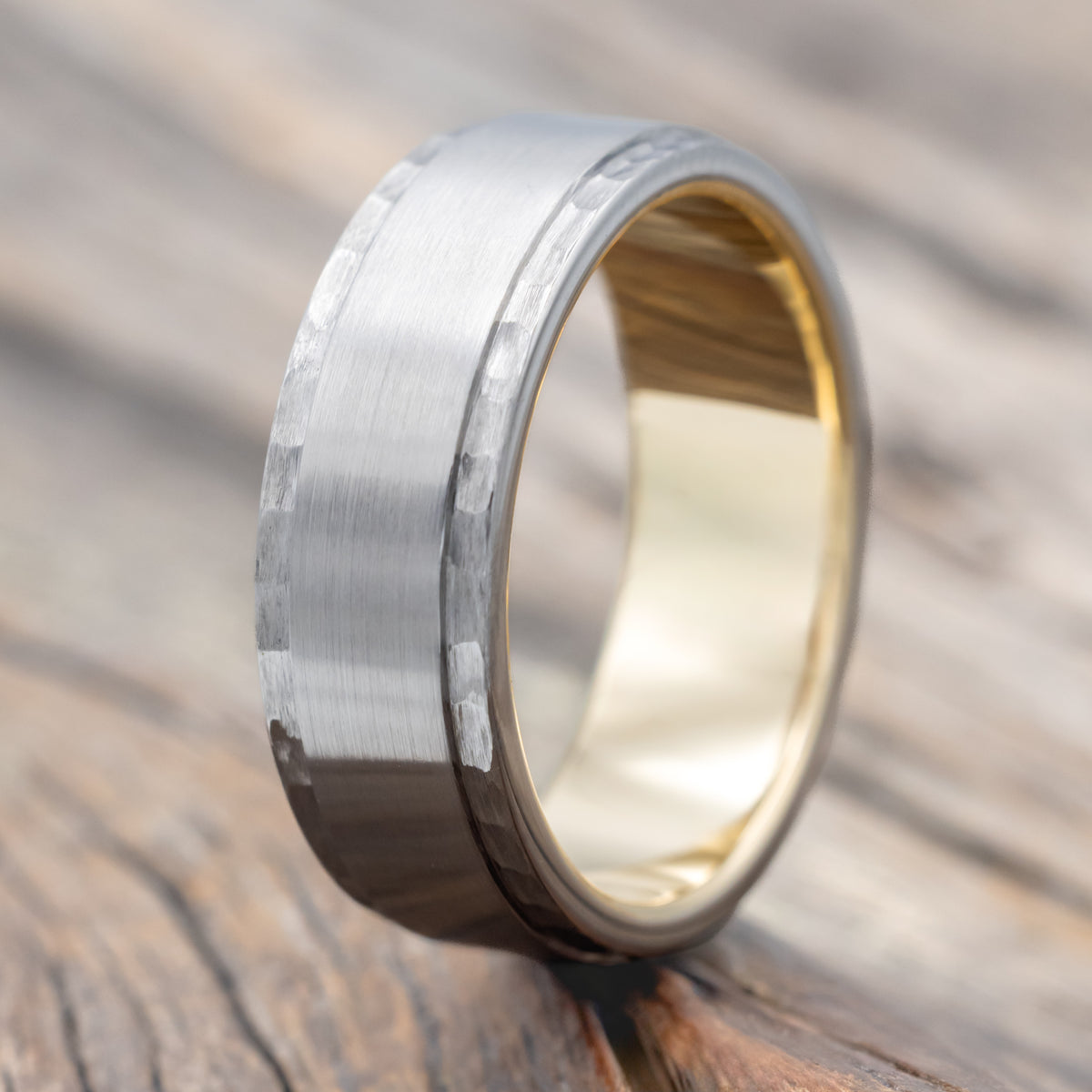 A titanium wedding ring with brushed center and hammered edges with gold lining on a wooden surface