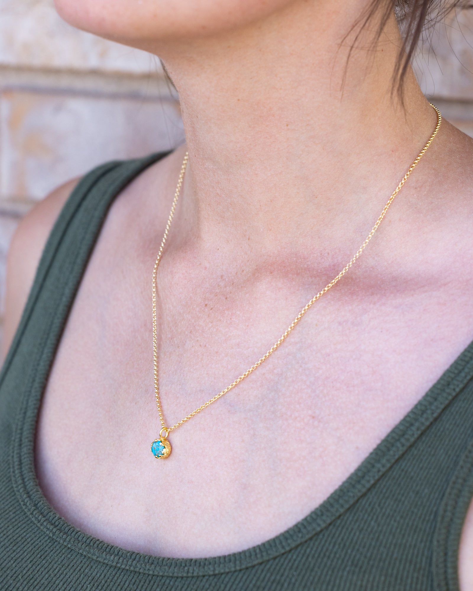 Gold necklace with a turquoise worn by a person in a green tank top.