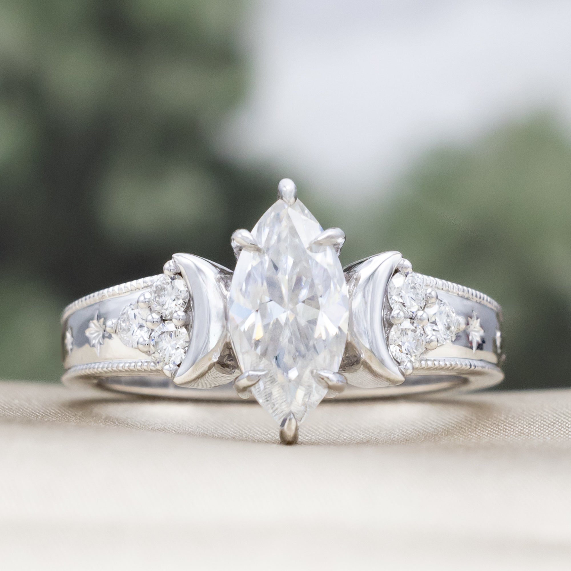 White gold ring with a large central moissanite and diamond accents on the band against a blurred green background
