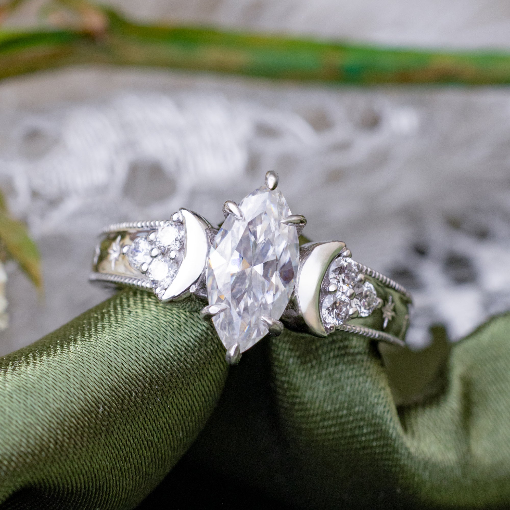 White gold engagement ring with crescent moon accents on green fabric 