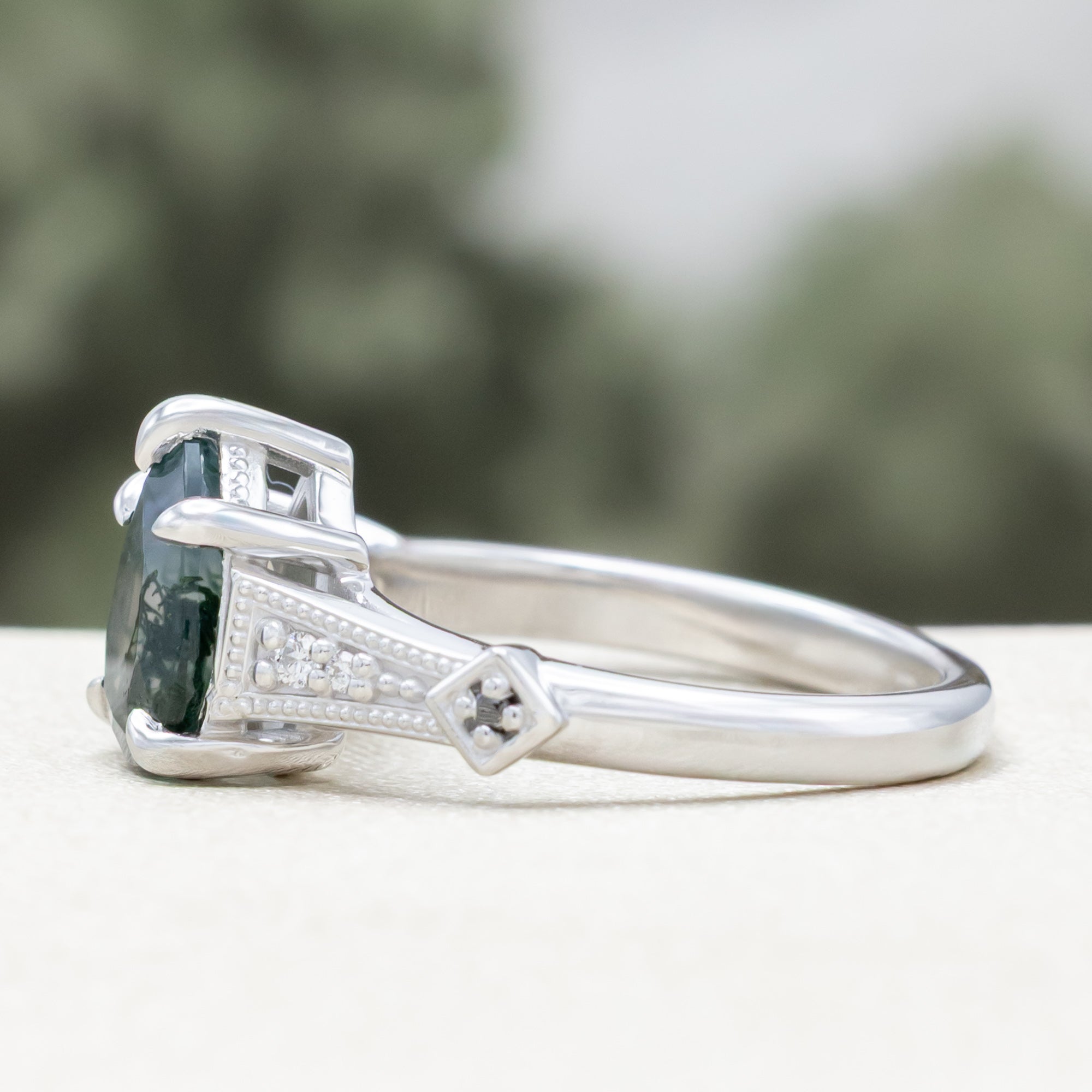 White gold engagement ring with moss agate and diamond accents on a blurred background