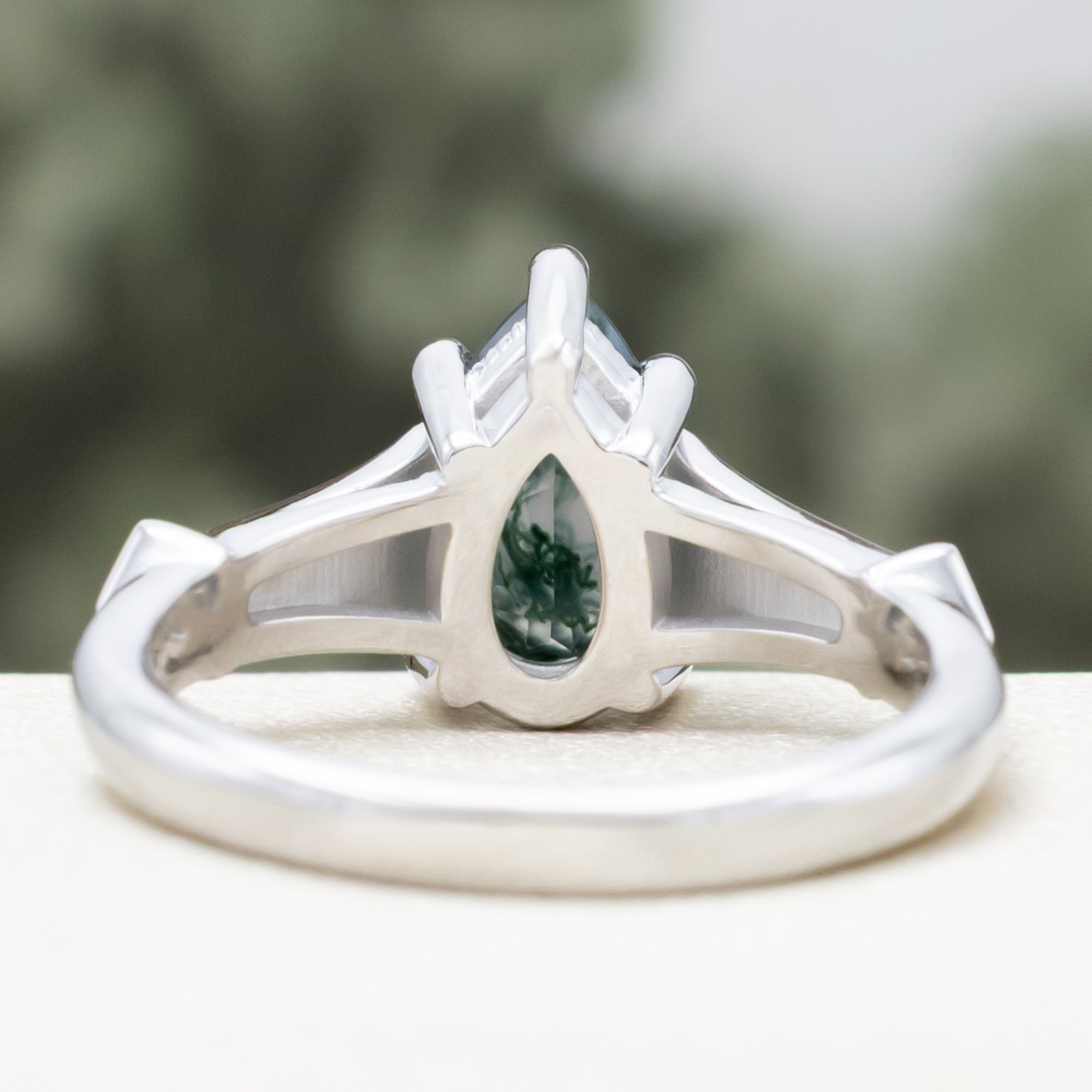 White gold engagement ring with moss agate and diamond accents on a blurred background