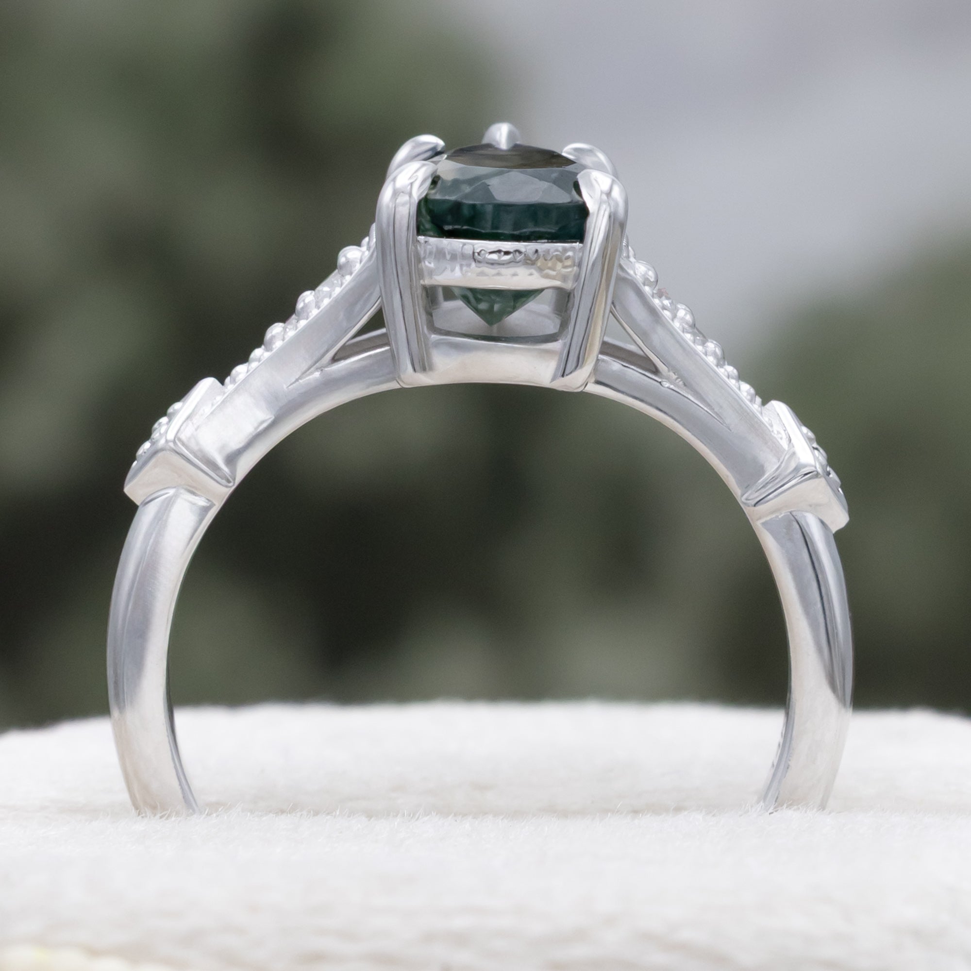 White gold engagement ring with moss agate and diamond accents on a blurred background