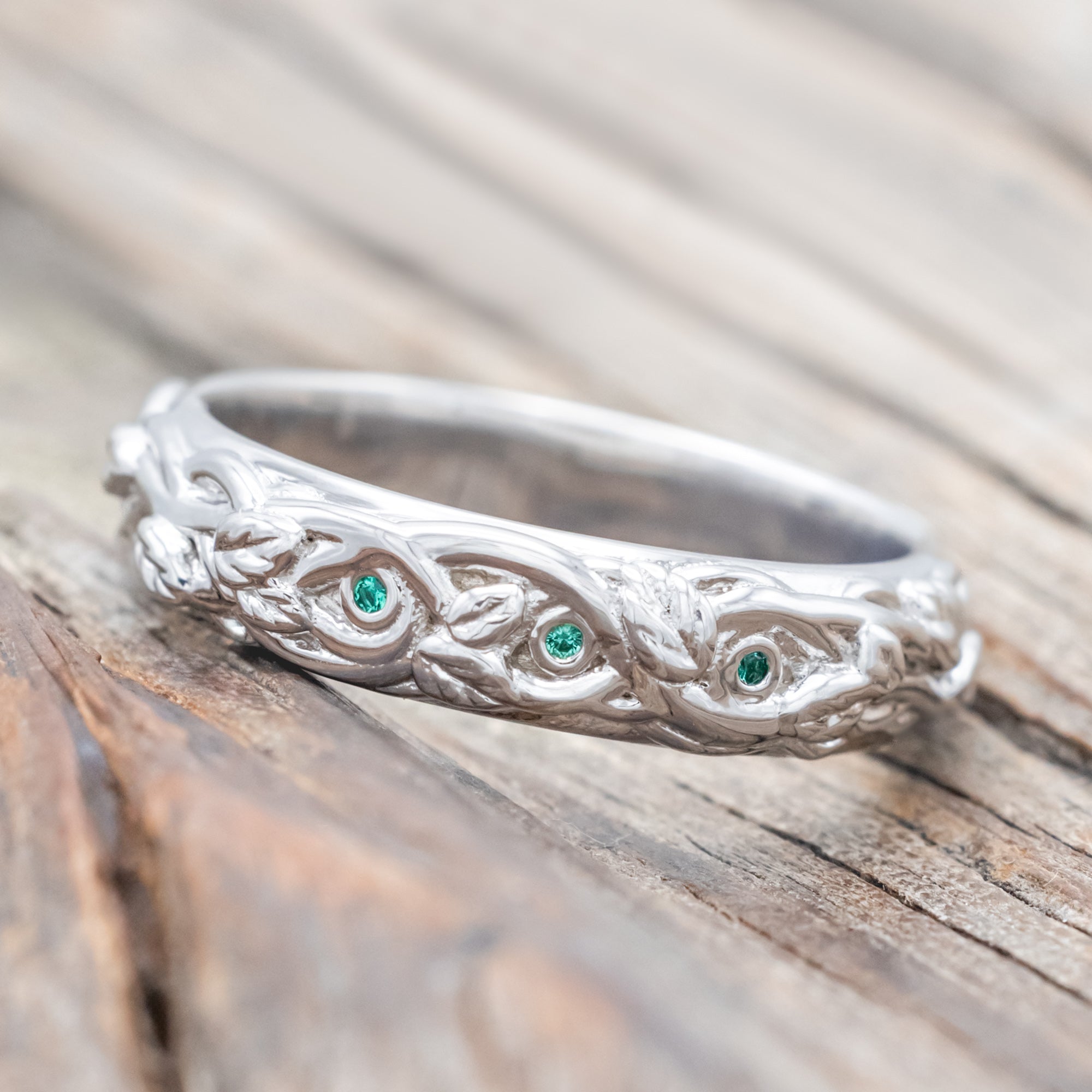 14K white gold ring with green emeralds and vine design on a wooden surface