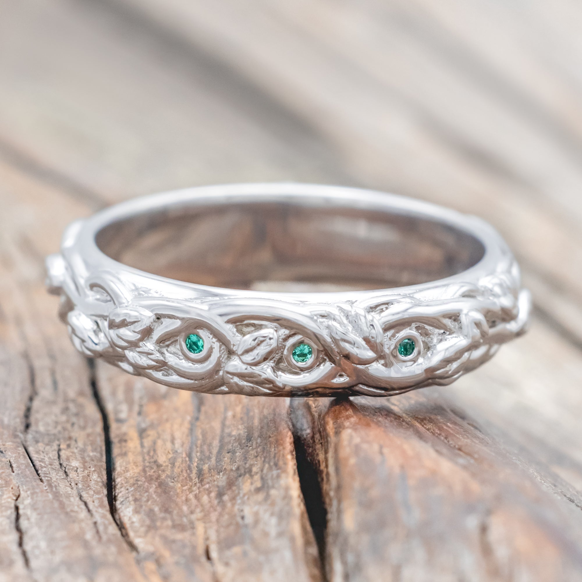 14K white gold ring with green emeralds and vine design on a wooden surface