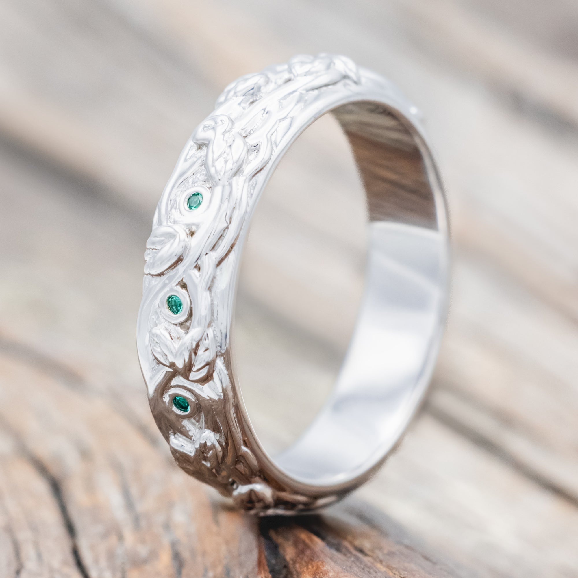 14K white gold ring with green emeralds and vine design on a wooden surface
