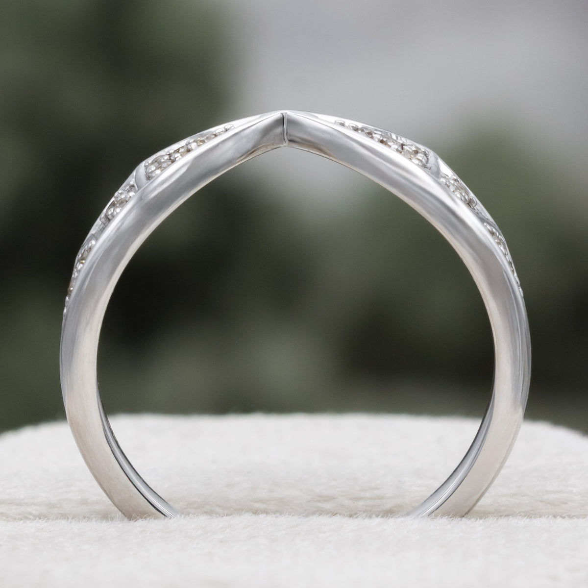 White gold bat wing wedding ring tracer with champagne diamond accents against a blurred green background