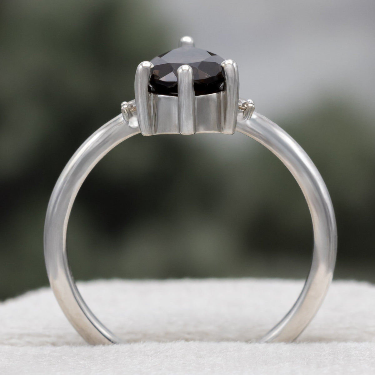 White gold engagement ring with smoky quartz center stone with champagne diamond accents against a blurred green background