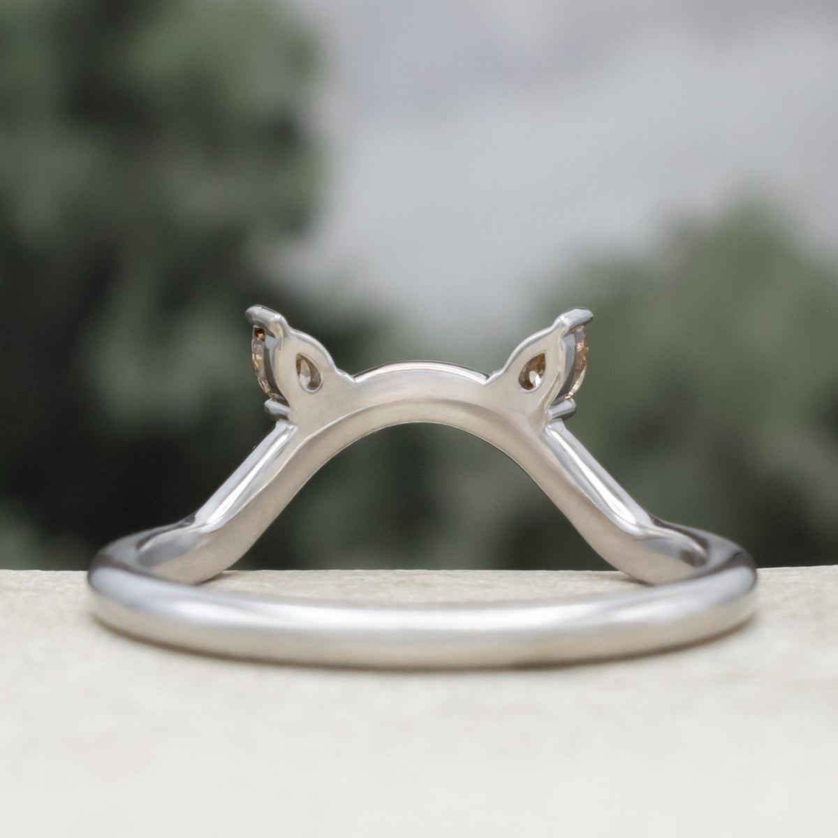 White gold cat ear wedding ring tracer with champagne diamond accents against a blurred green background