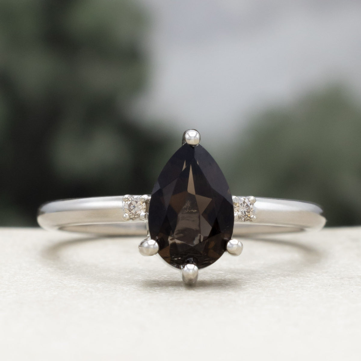 White gold engagement ring with smoky quartz center stone with champagne diamond accents against a blurred green background