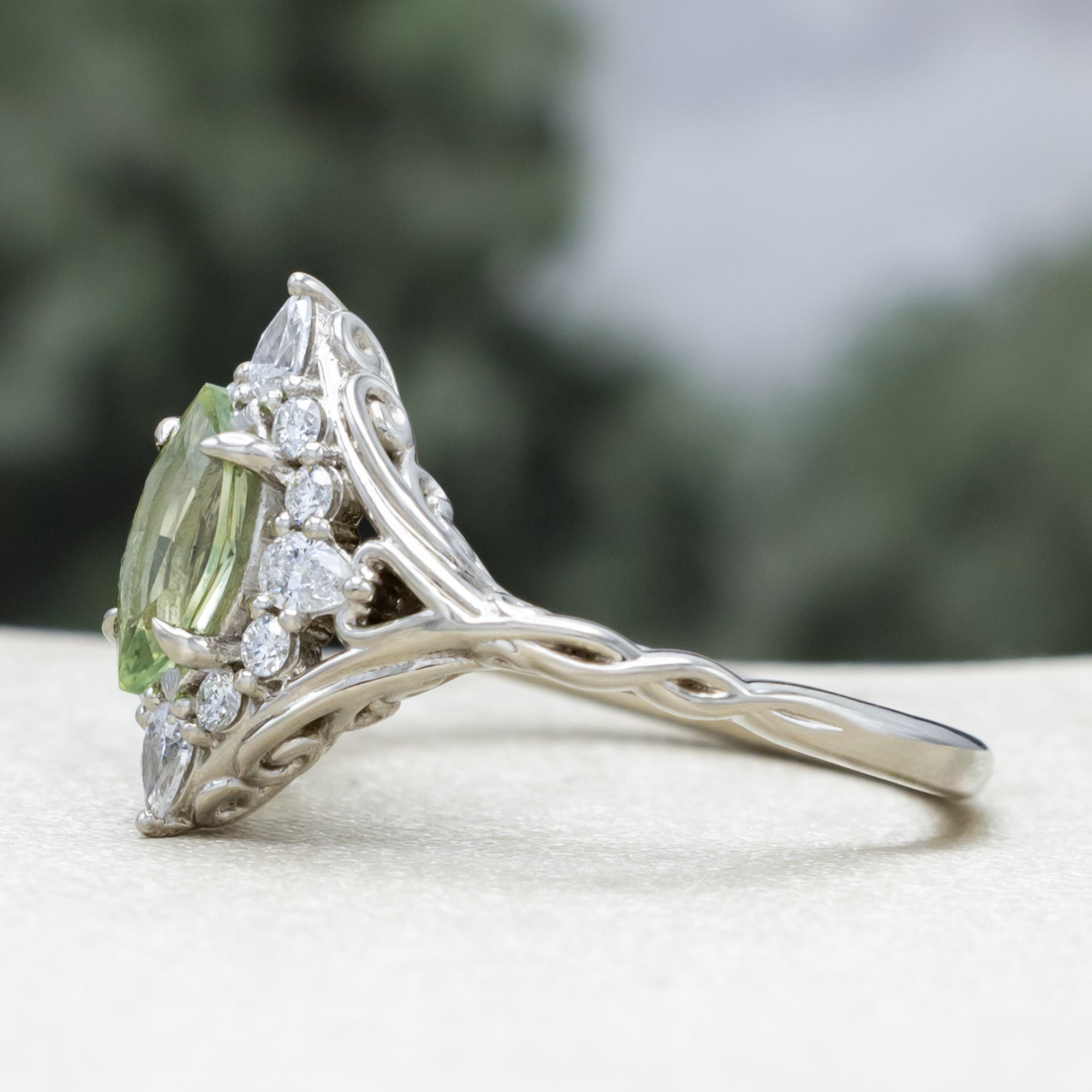 White gold ring with a green sapphire and diamond halo on a neutral background