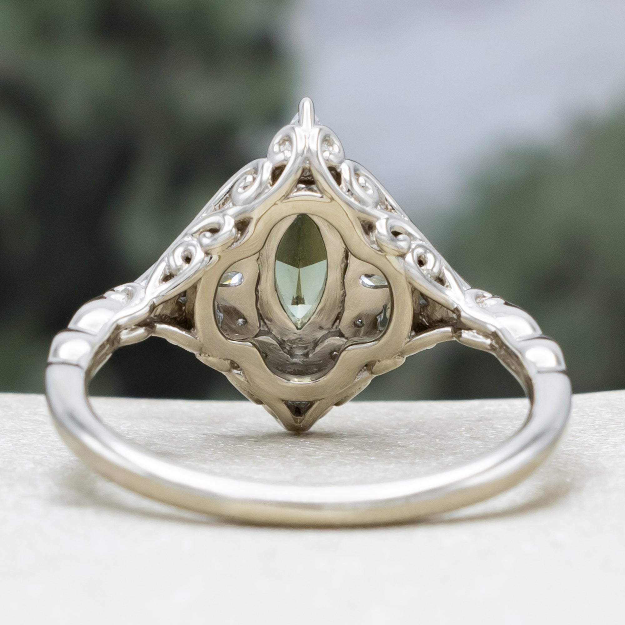 White gold ring with a green sapphire and diamond halo on a neutral background
