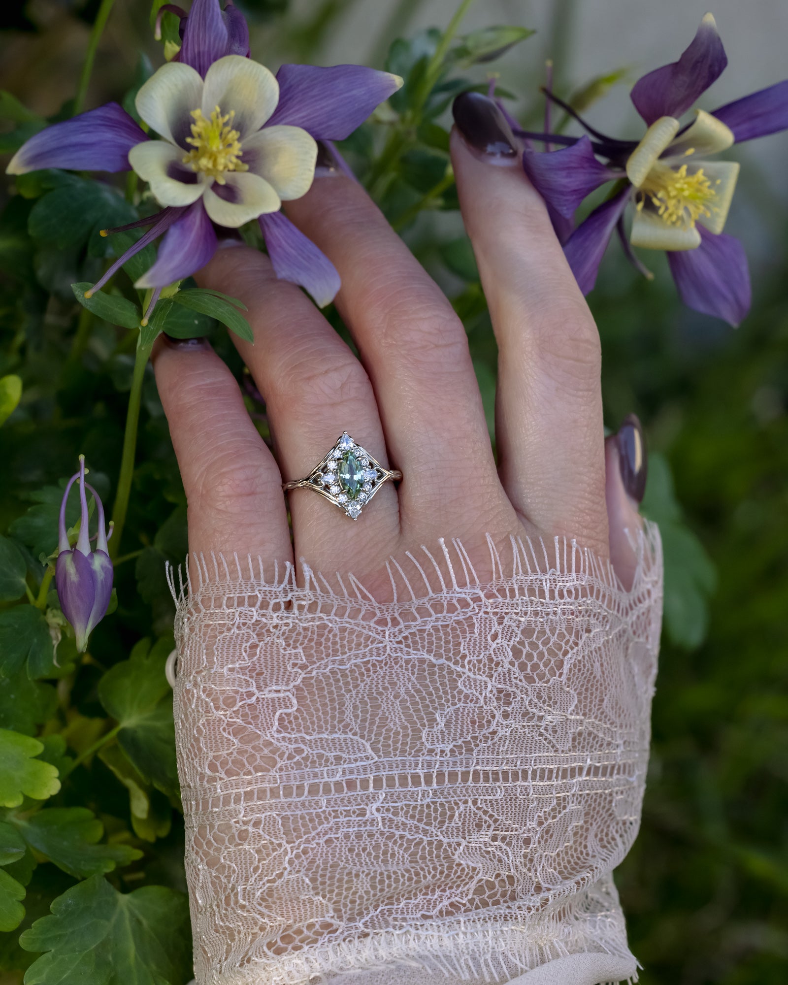 Hand wearing a green sapphire ring with purple flowers in the background