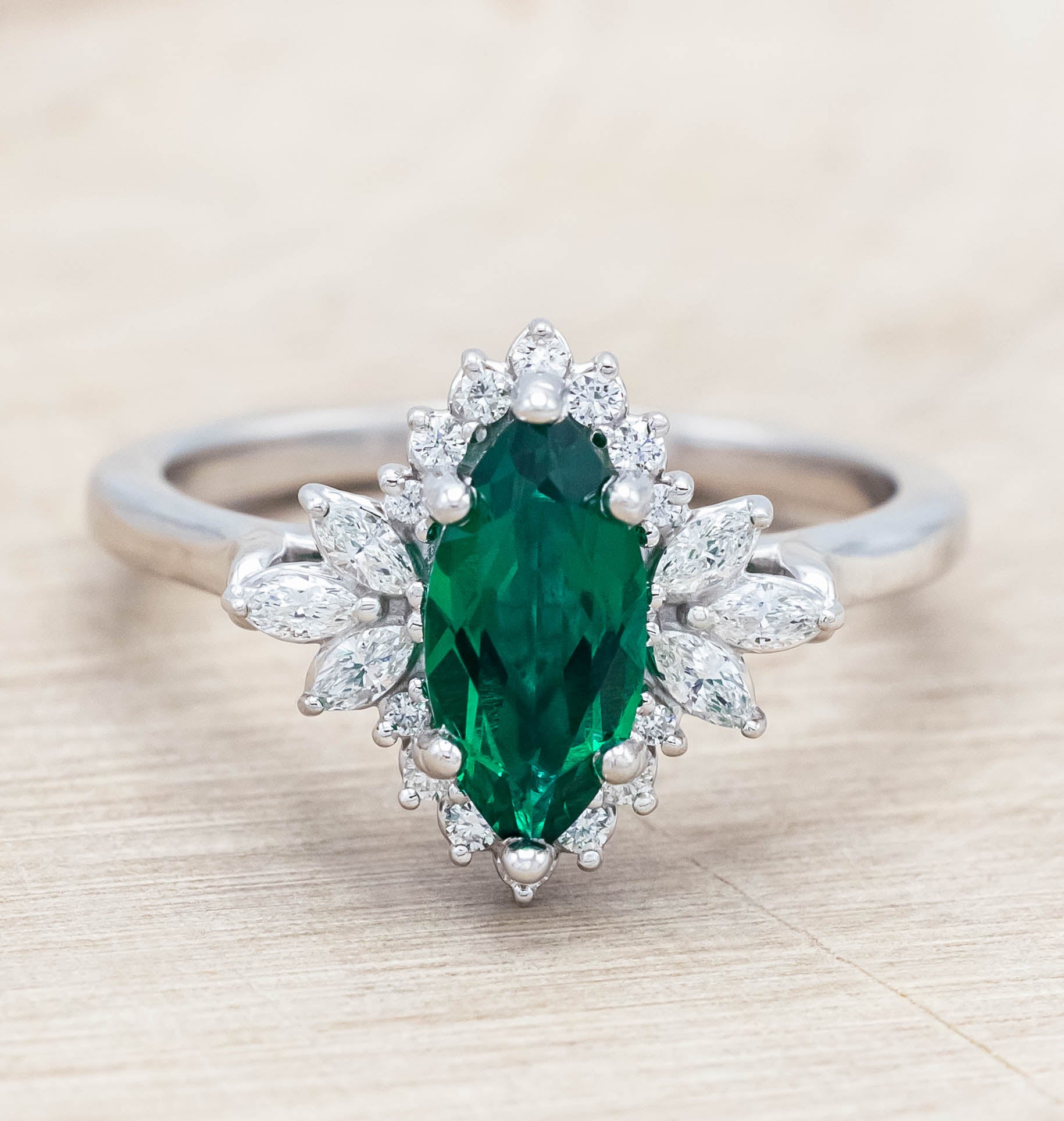 14K white gold ring with a green emerald on a light wooden background
