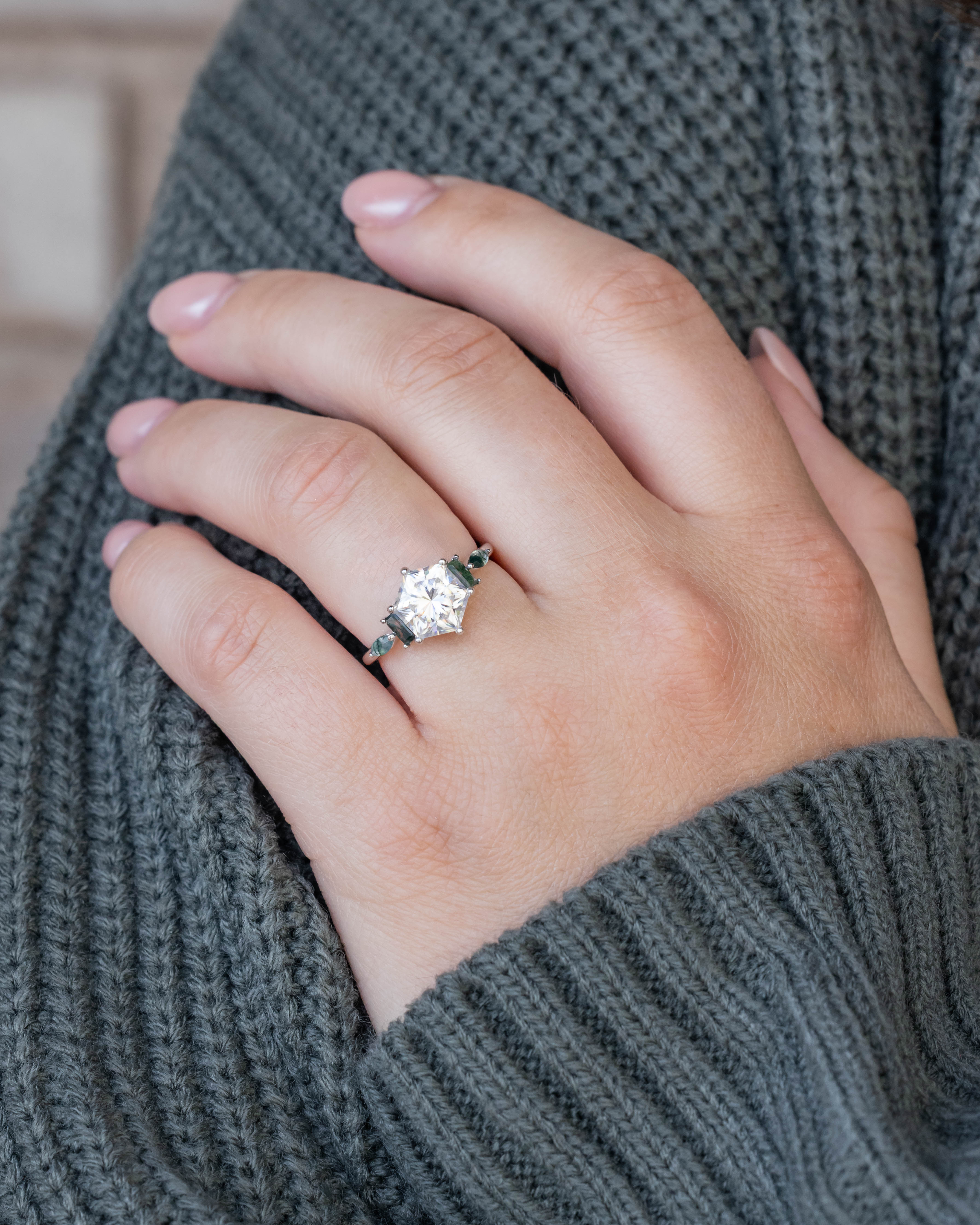 Hand wearing a moissanite ring with a blurred background