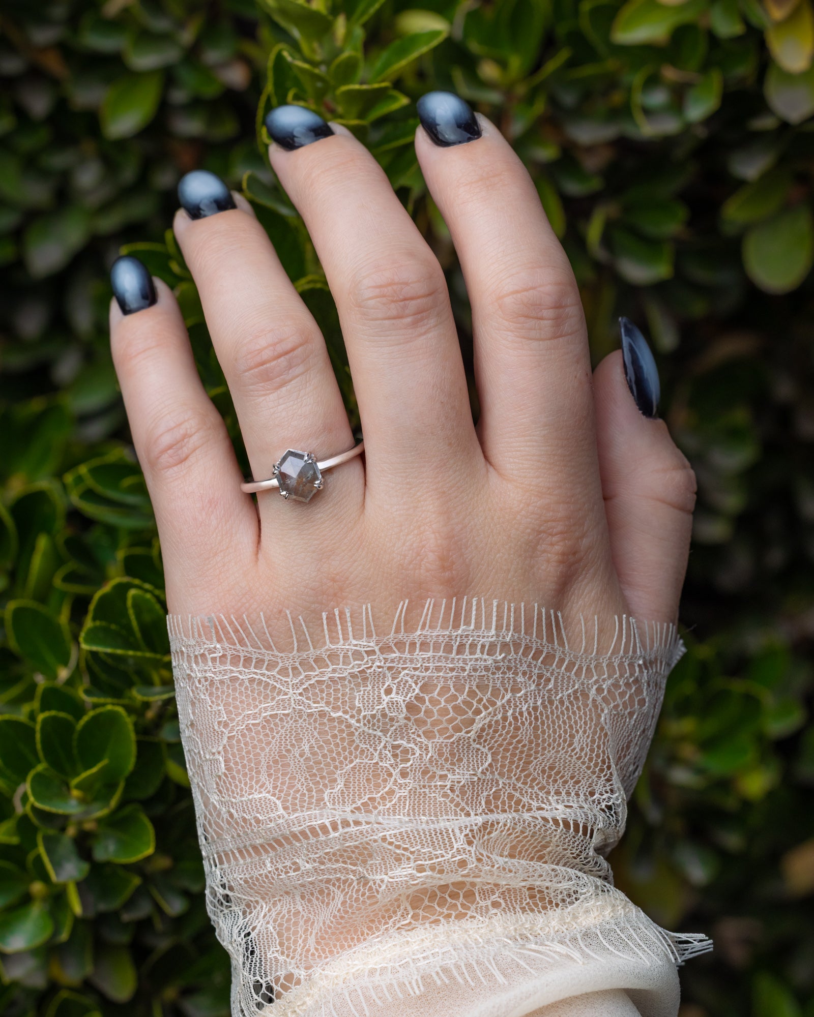 Hand wearing a salt & pepper ring with a green leafy background