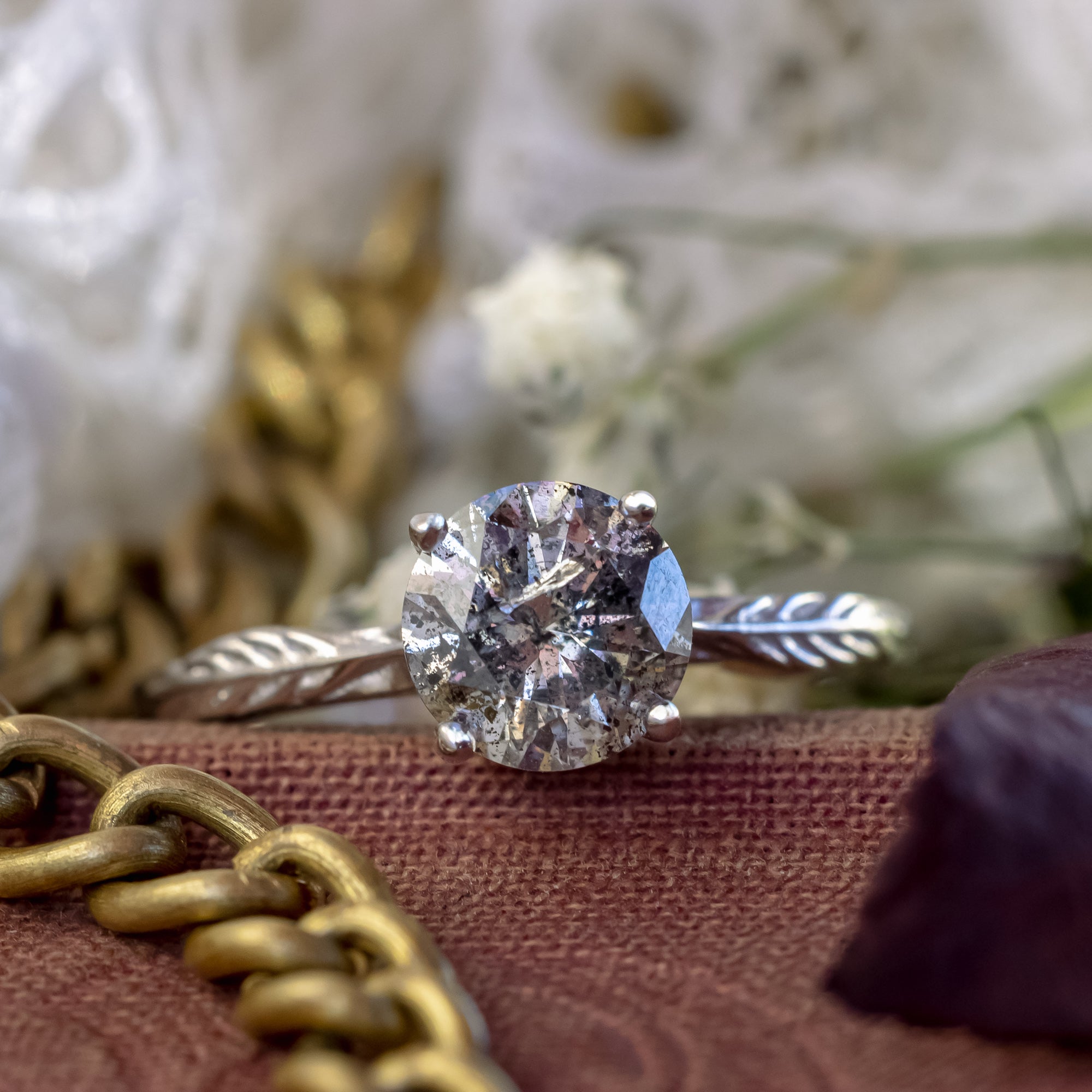 White gold ring with salt & pepper diamond on a blurred decorative surface