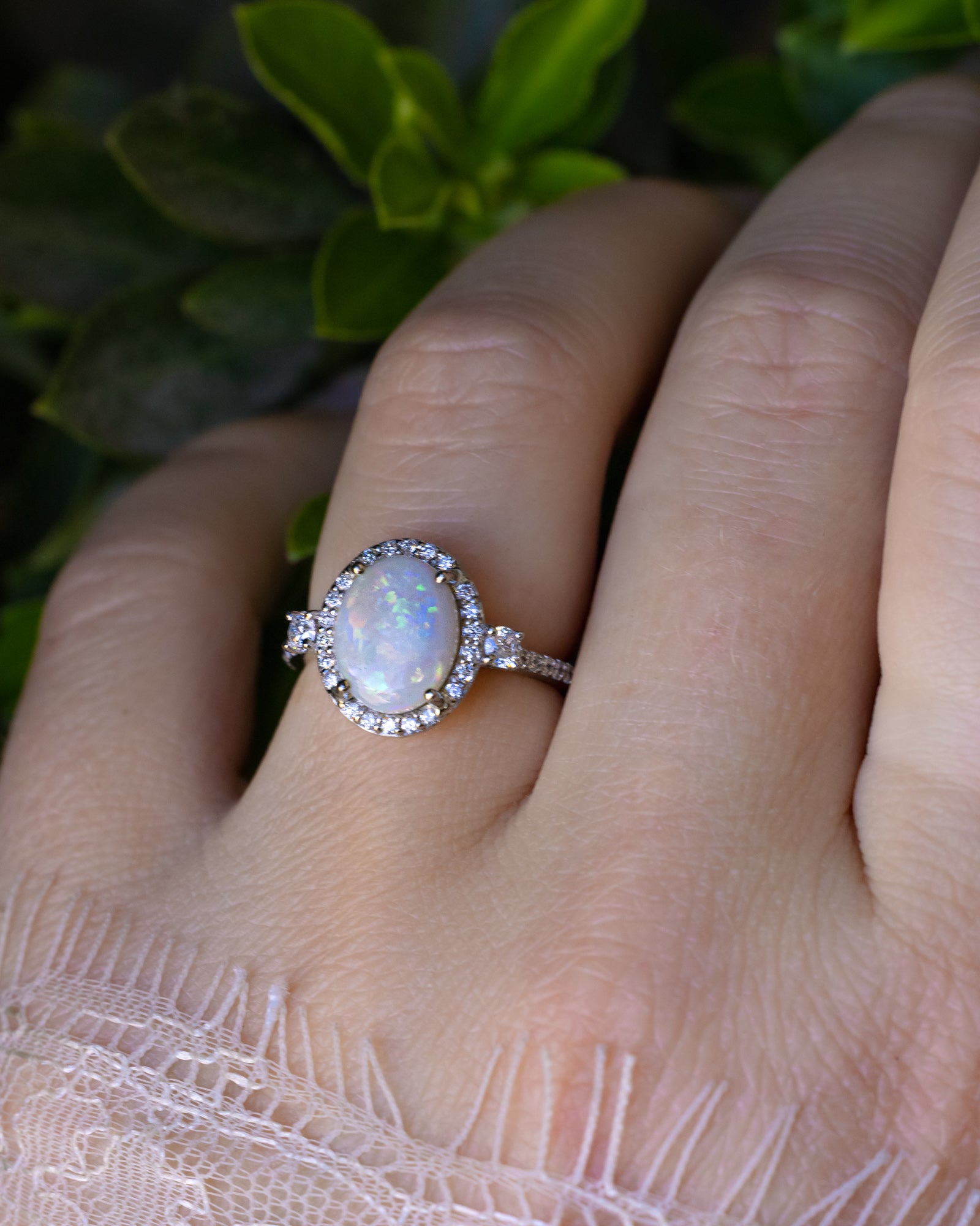 Ring with a large opal centerstone and diamond accents on a hand against a green blurred background