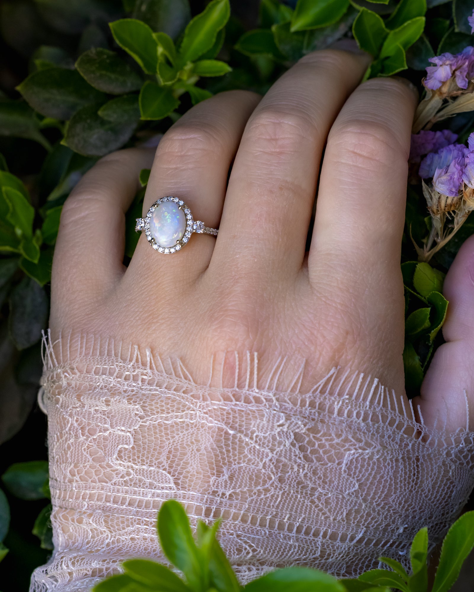 Ring with a large opal centerstone and diamond accents on a hand against a natural background