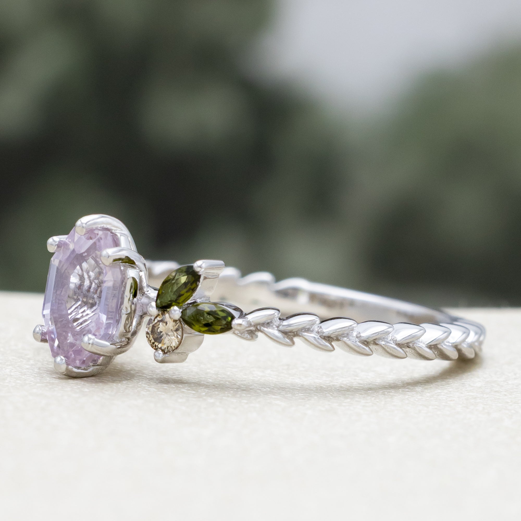 White gold pink sapphire ring with champagne diamond & tourmaline accents against a blurred green background
