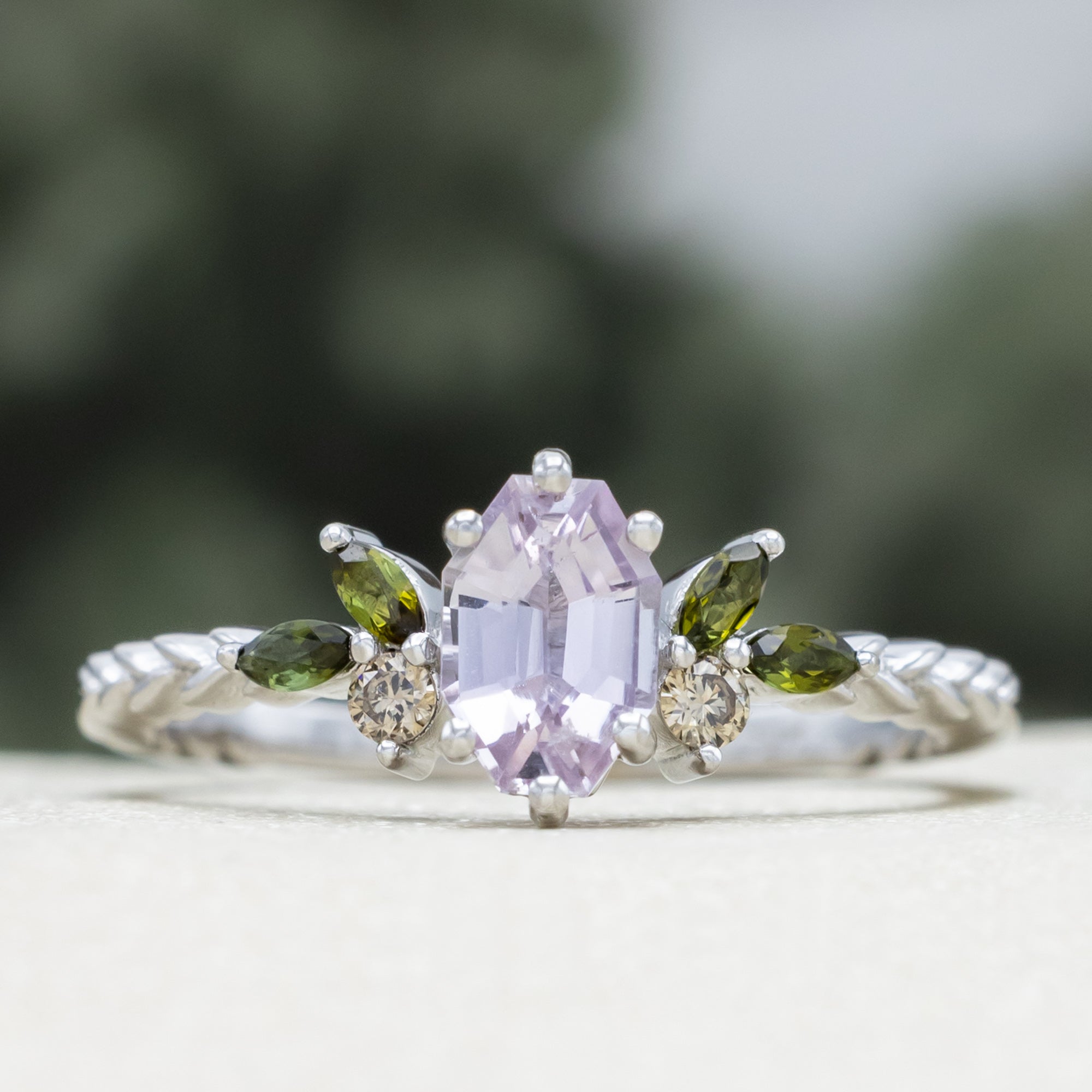 White gold pink sapphire ring with champagne diamond & tourmaline accents against a blurred green background