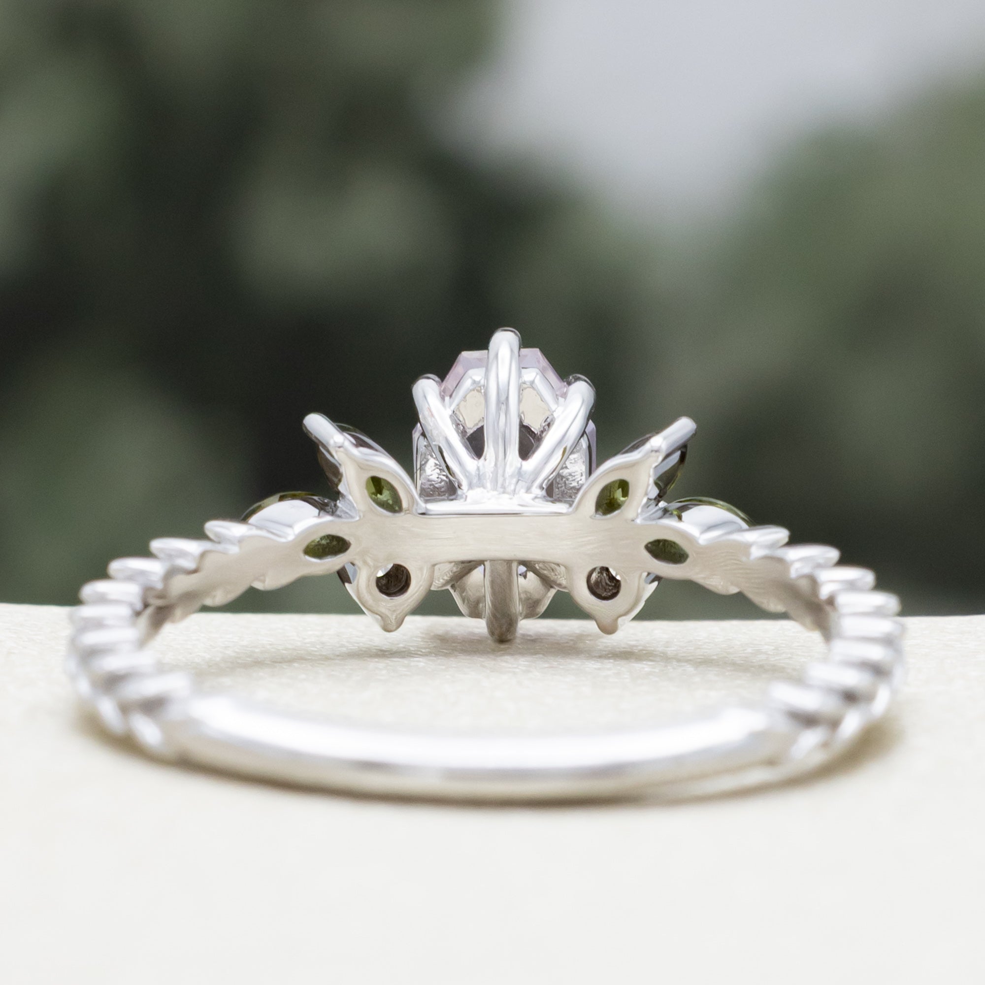 White gold pink sapphire ring with champagne diamond & tourmaline accents against a blurred green background