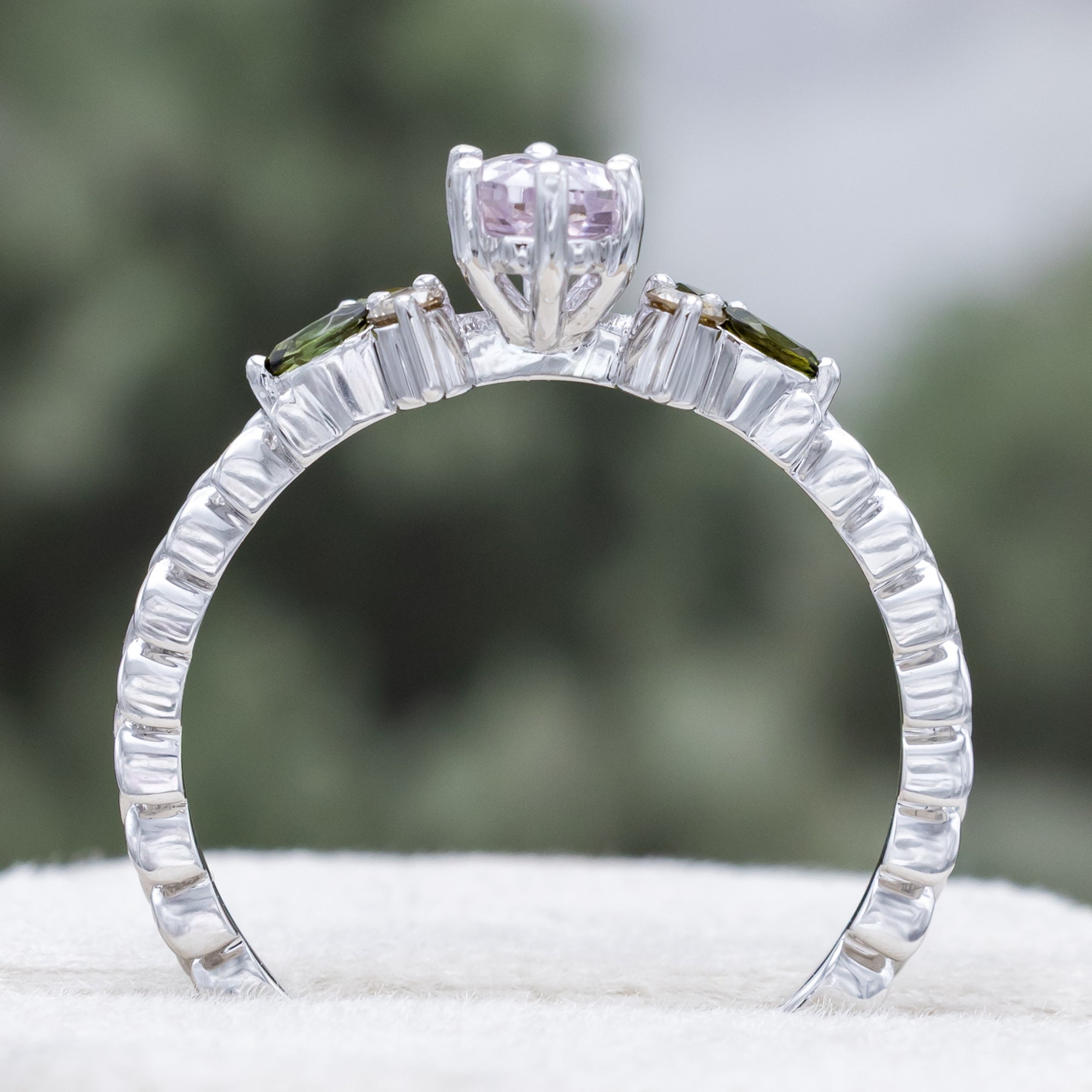 White gold pink sapphire ring with champagne diamond & tourmaline accents against a blurred green background