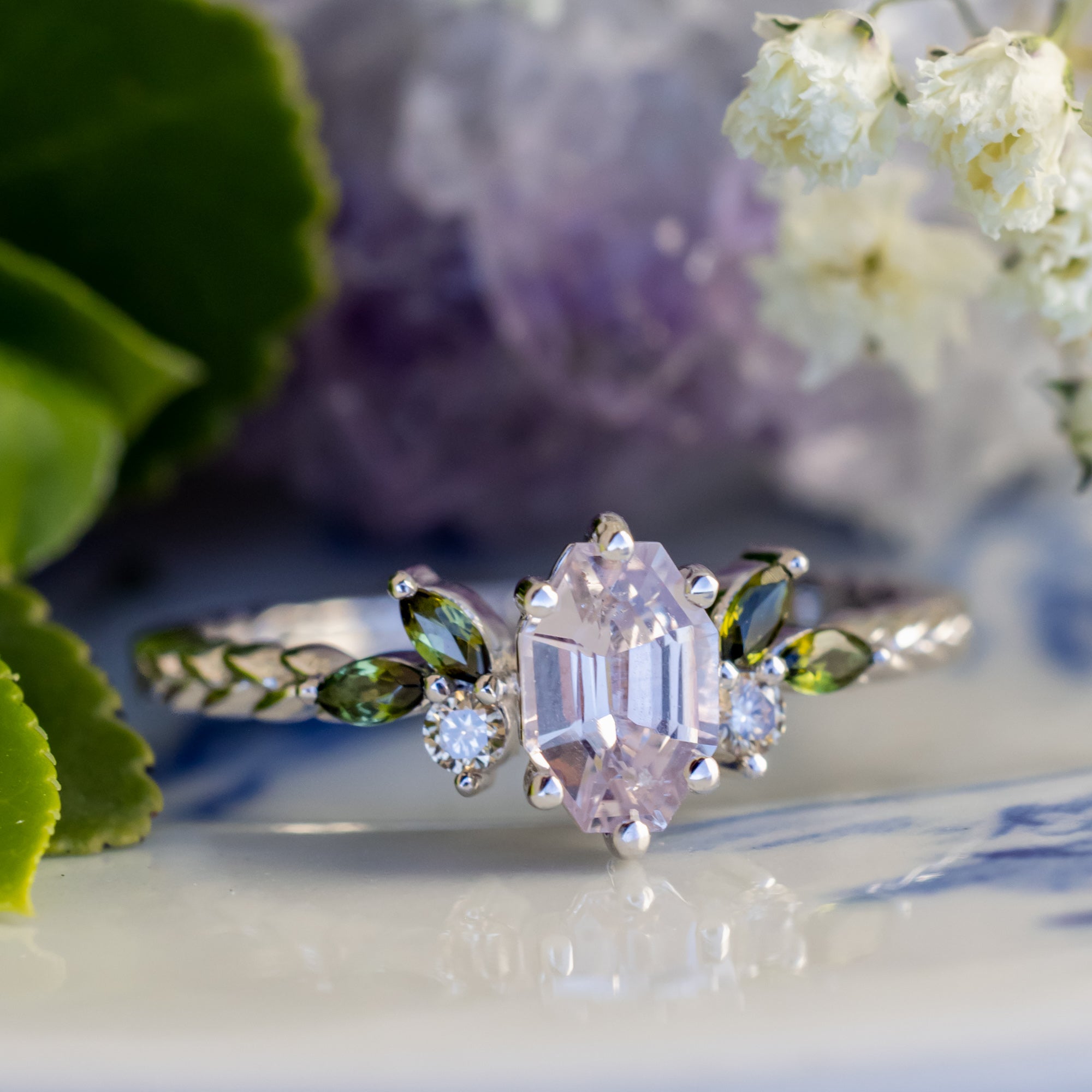 White gold ring with pink sapphire center stone on a blurred floral background