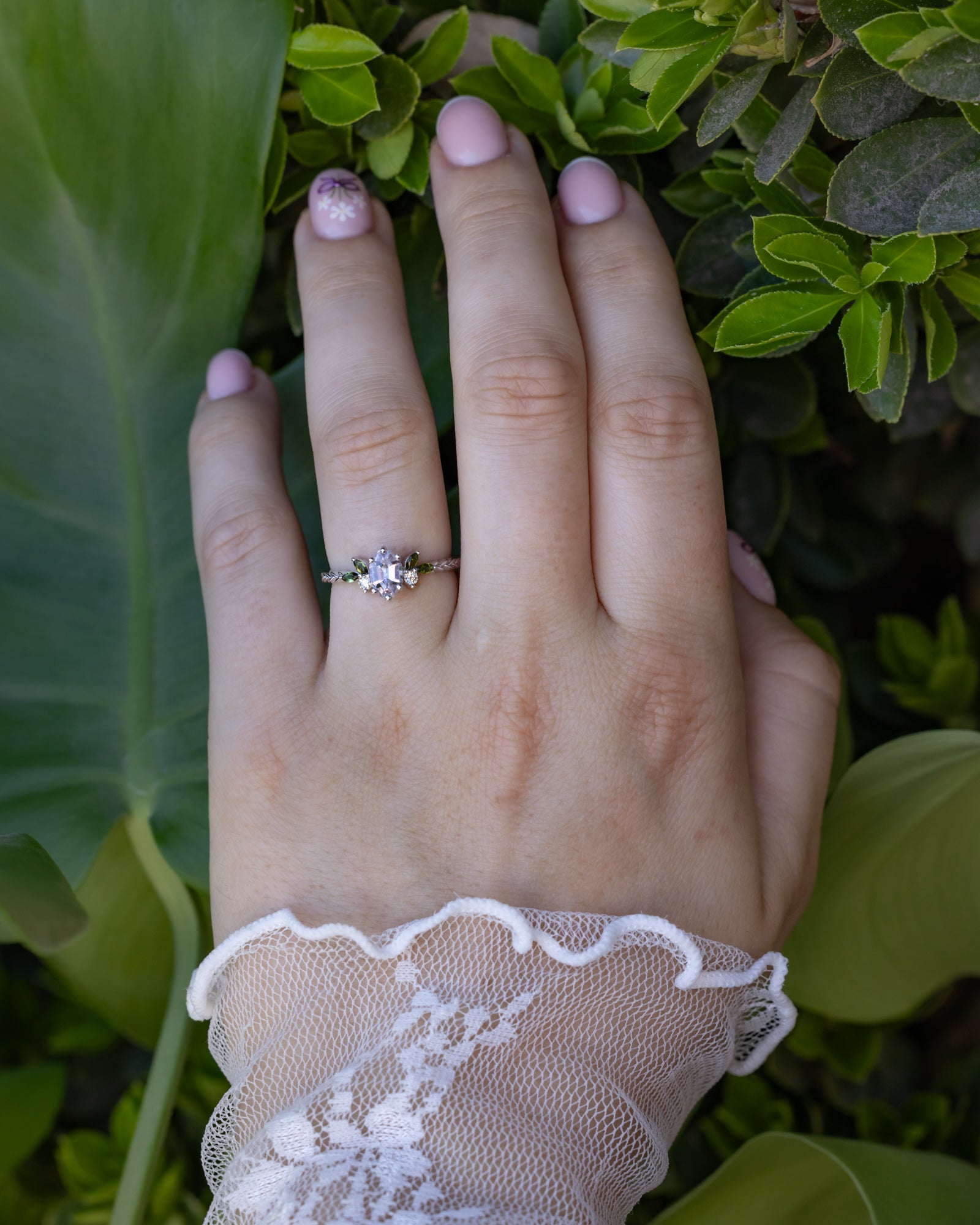 Hand wearing white gold ring with pink sapphire center stone on a blurred natural background