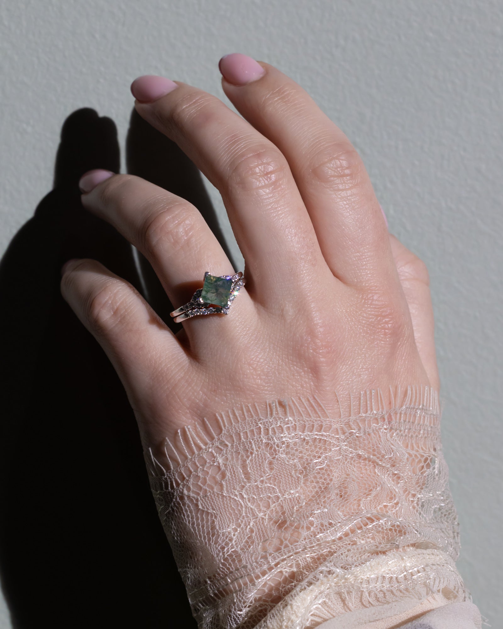 Hand wearing a ring with a moss agate center stone against a neutral background