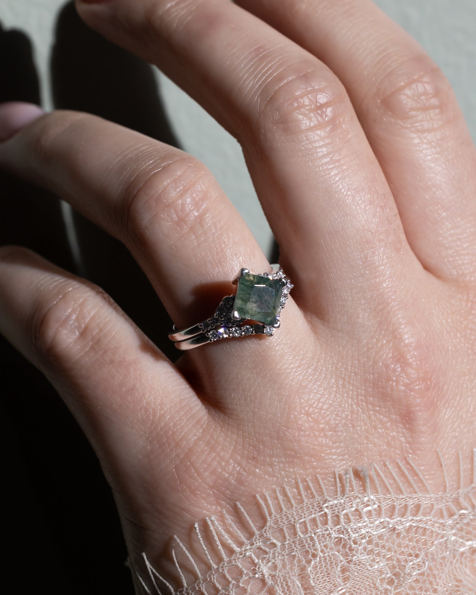 Hand wearing a ring with a moss agate center stone on a plain background