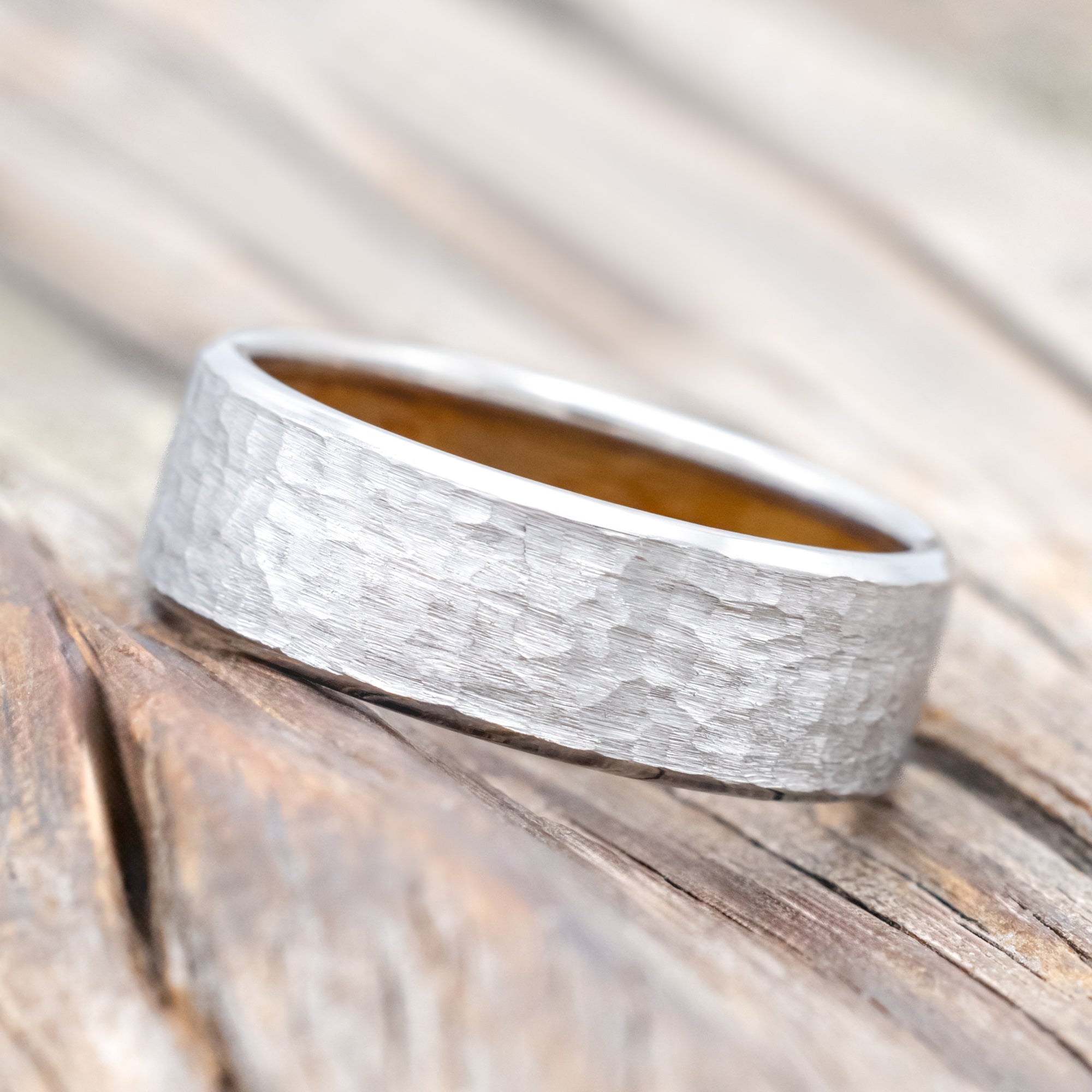 Hammered white gold ring with whiskey barrel oak lining on a wooden surface