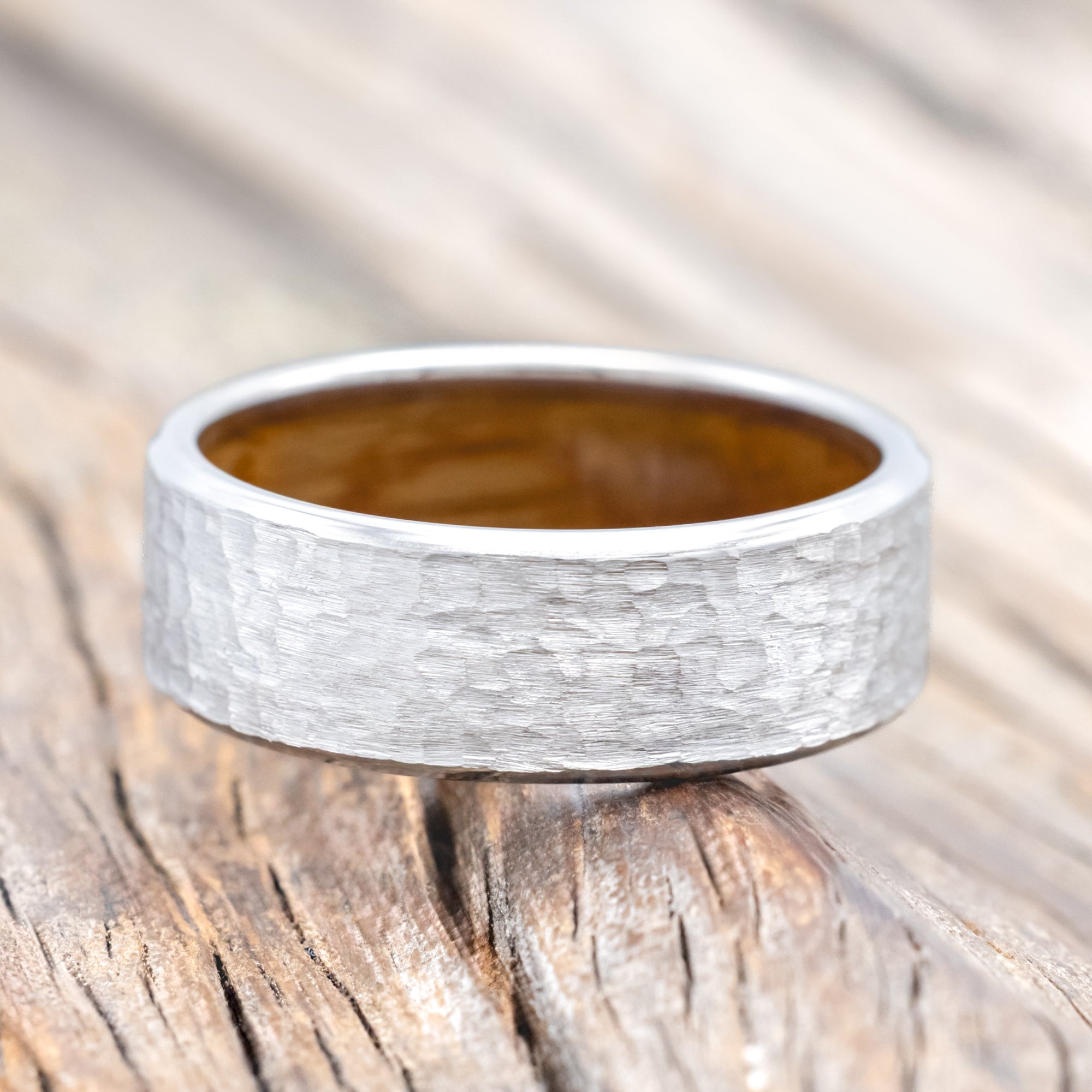 Hammered white gold ring with whiskey barrel oak lining on a wooden surface