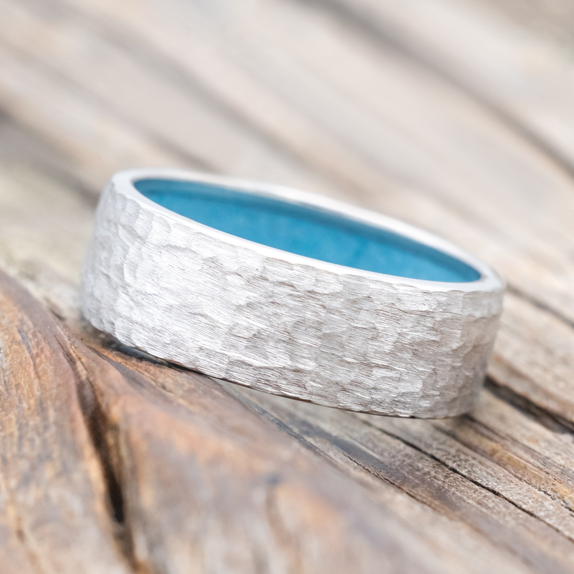 Hammered white gold ring with turquoise lining on a wooden surface