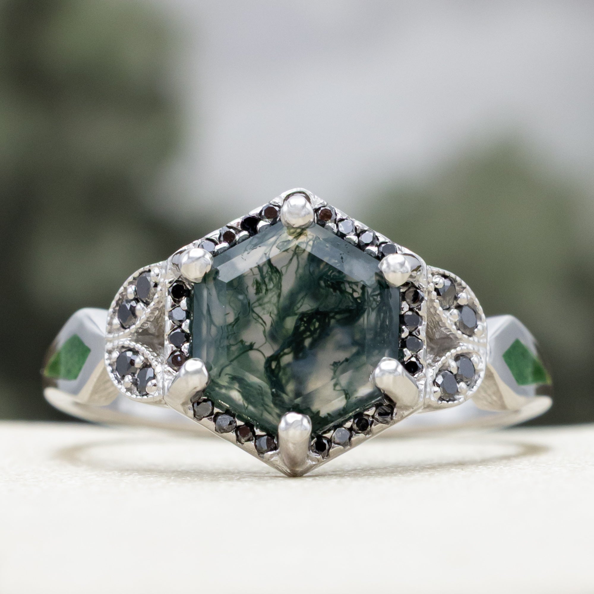 White gold ring with a moss agate center stone and black diamond accents on a blurred background