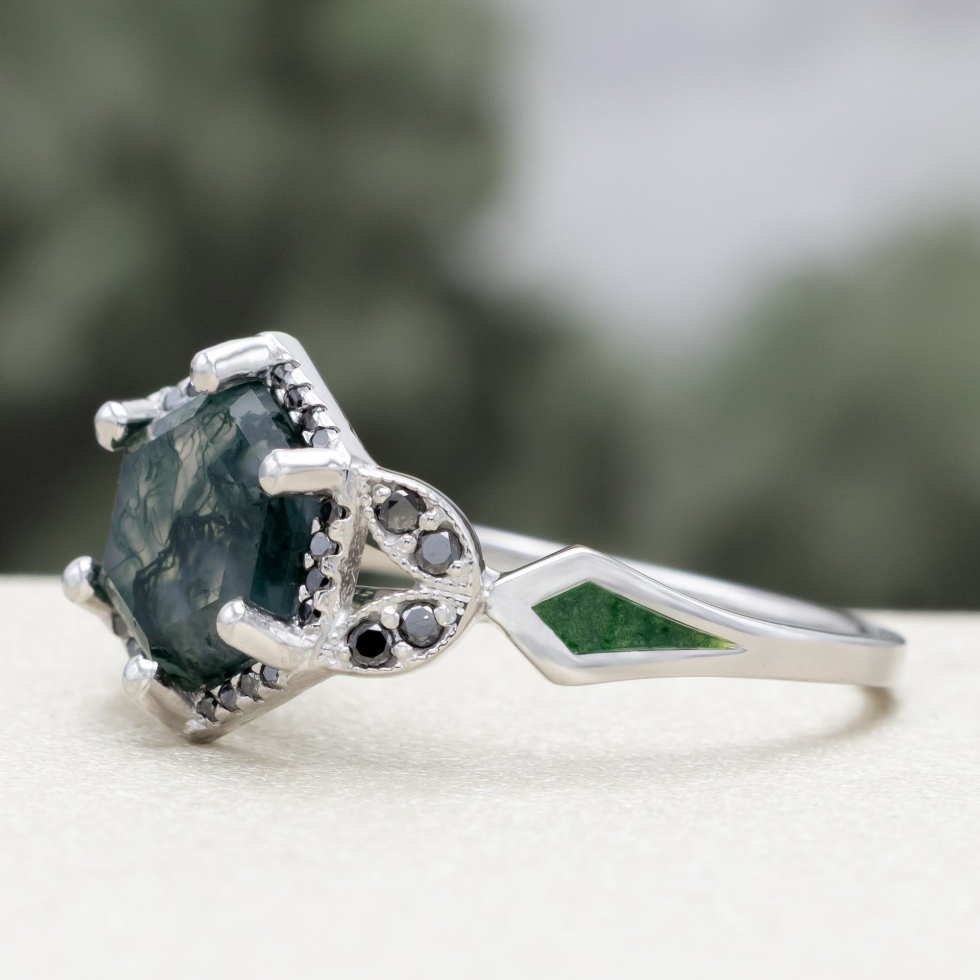 White gold ring with a moss agate center stone and black diamond accents on a blurred background