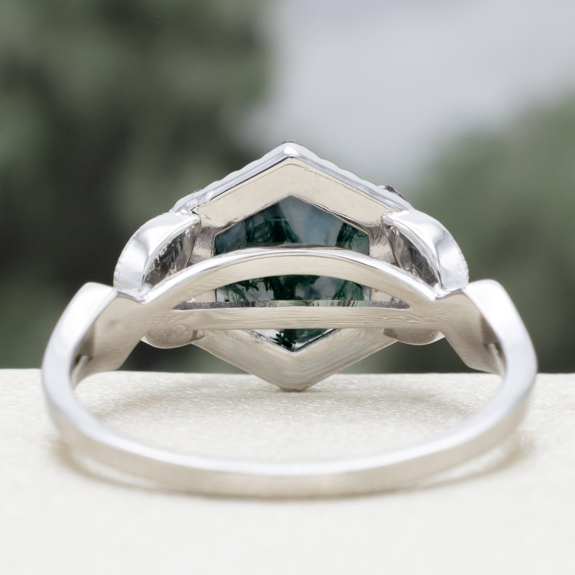 White gold ring with a moss agate center stone and black diamond accents on a blurred background