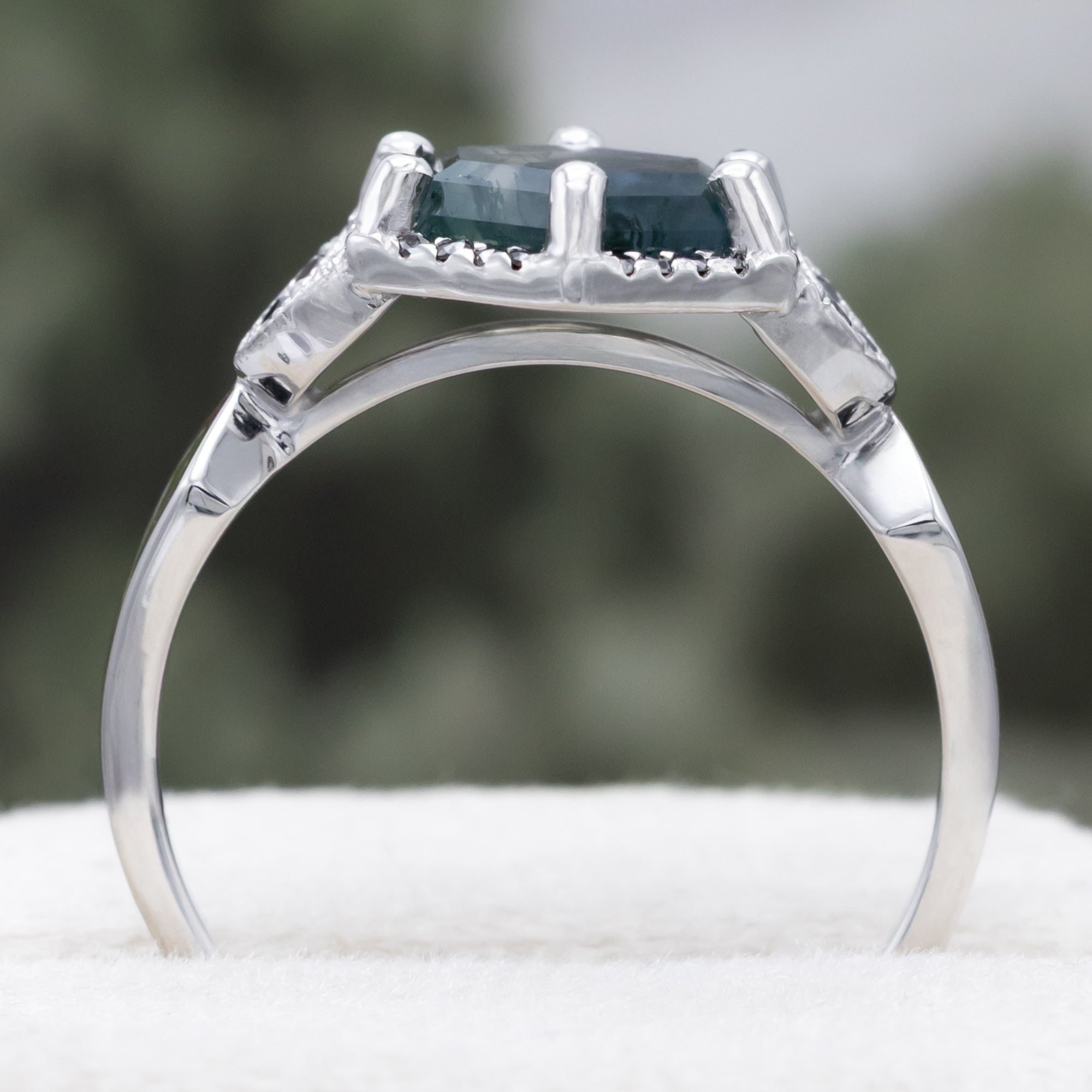 White gold ring with a moss agate center stone and black diamond accents on a blurred background