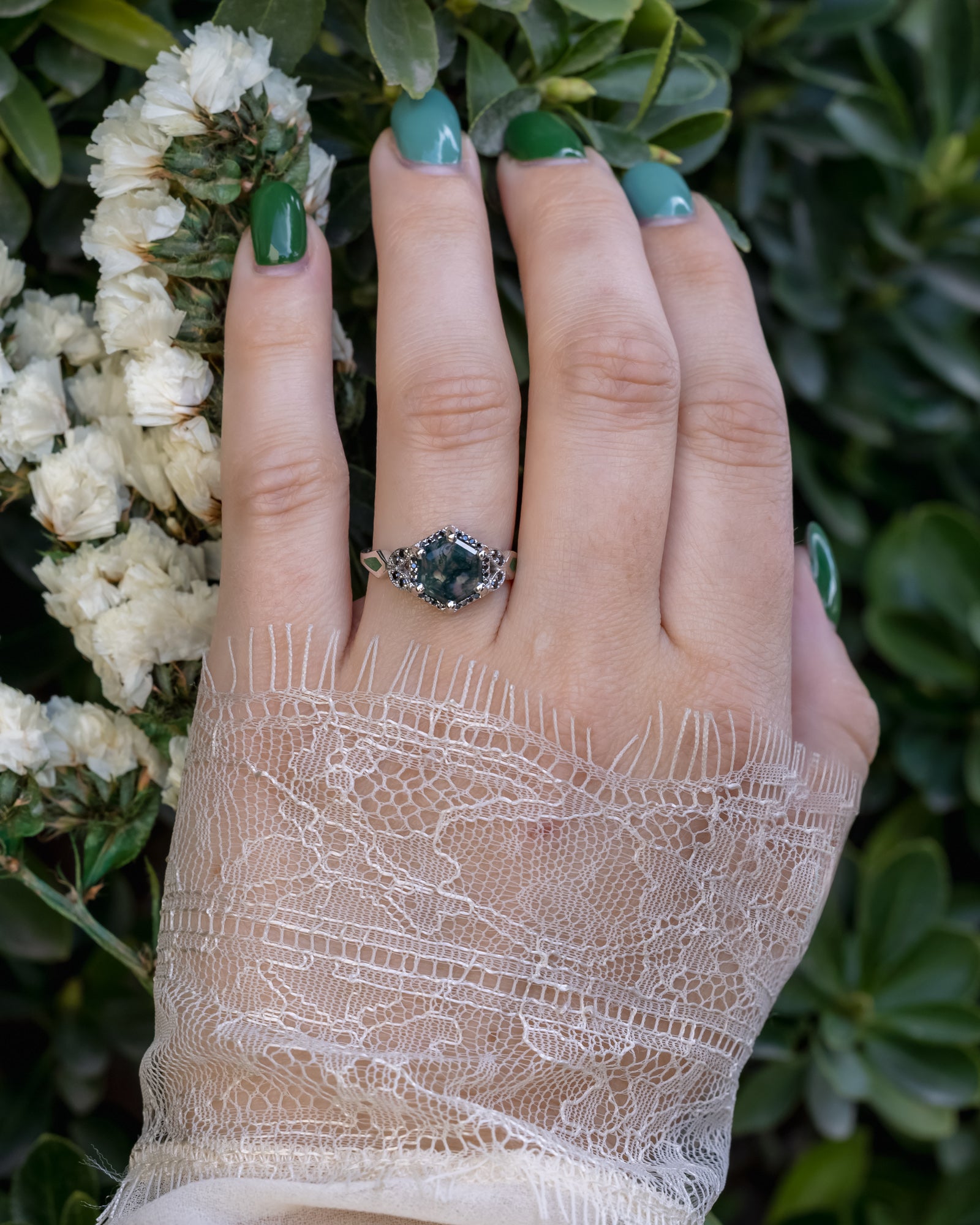 Hand wearing a ring with green nail polish against a natural background