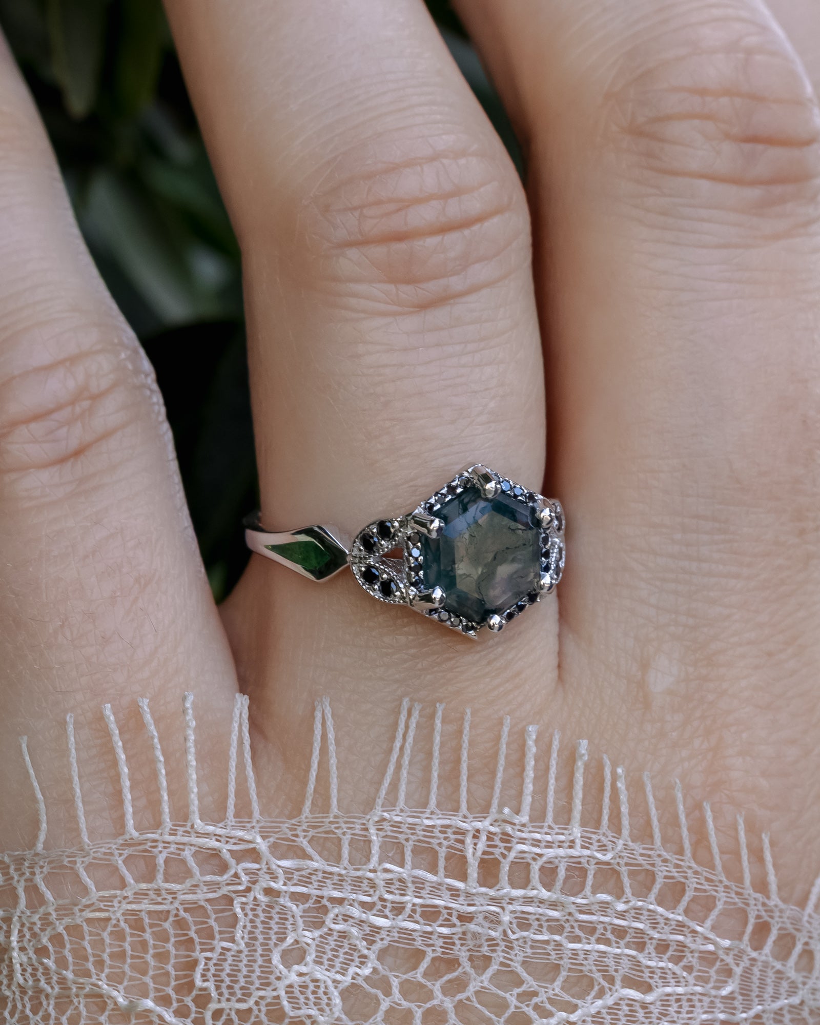 Ring with a moss agate centerstone on a finger against a lace sleeve