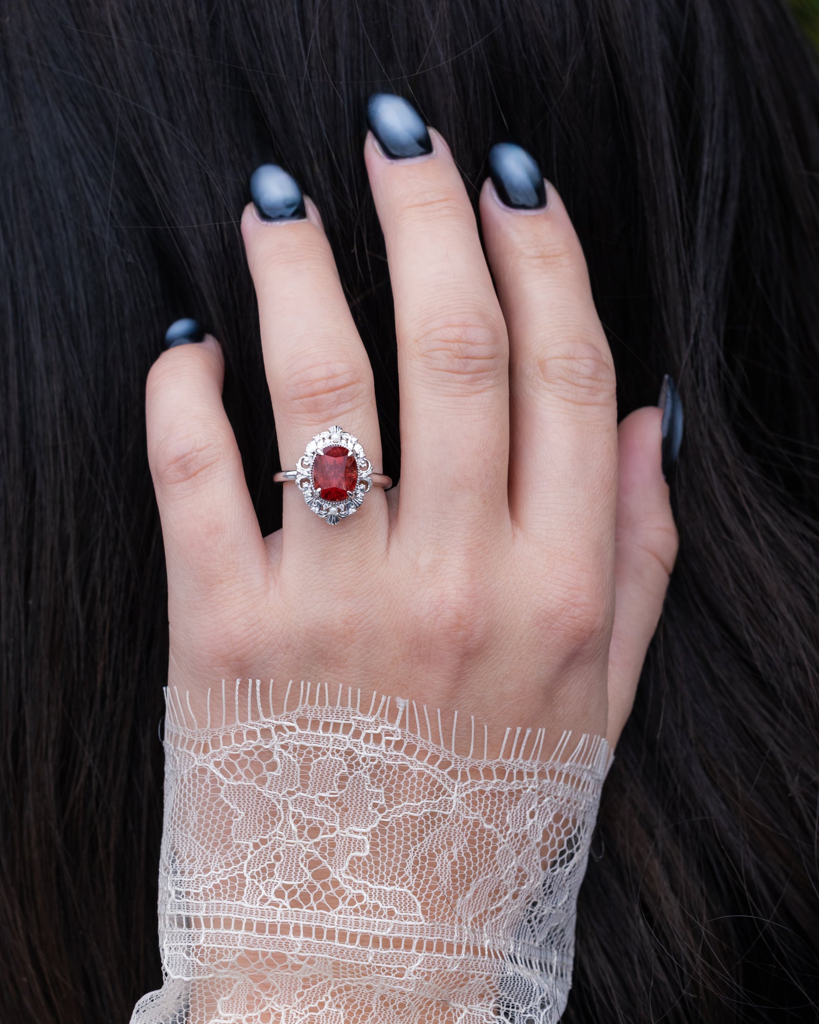 Hand wearing a ring with a red sunstone against a dark background