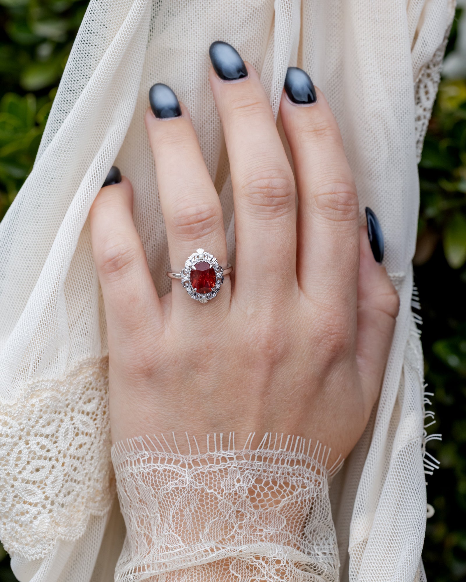 Hand wearing a ring with a red sunstone, set against a white lace fabric.