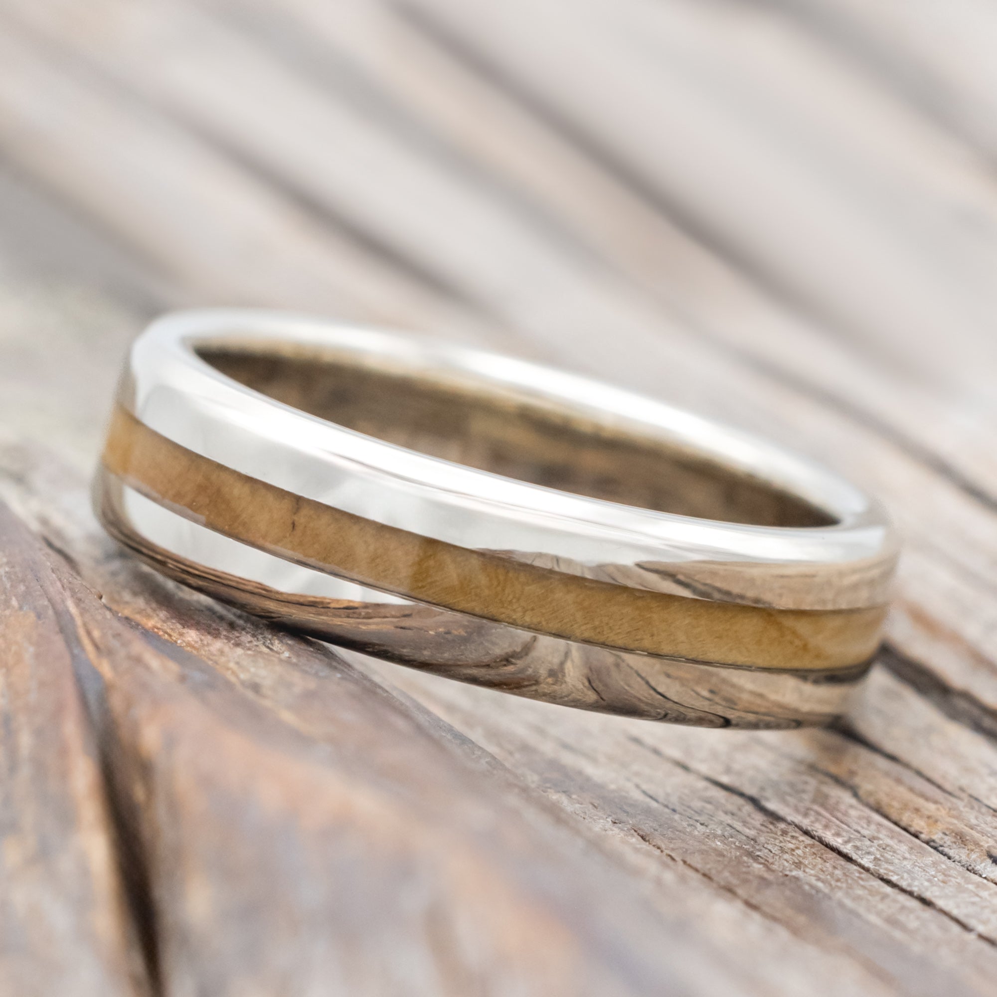 14K white gold and fig wood ring on a wooden surface with a blurred background