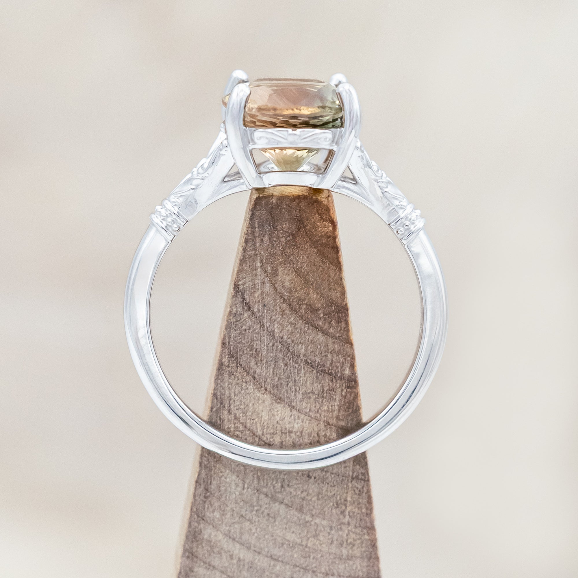 White gold ring with a sunstone on a wooden stand against a beige surface
