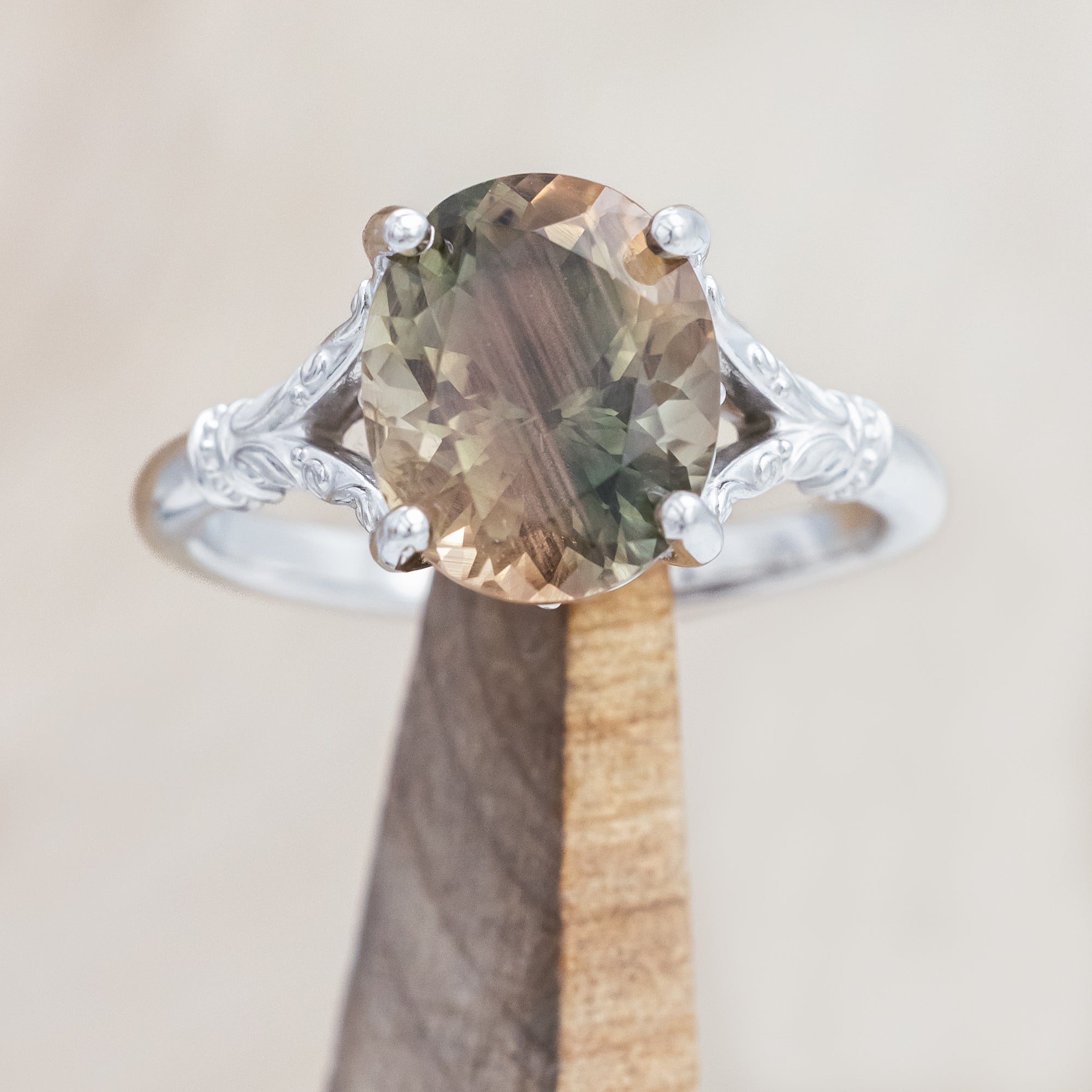 White gold ring with a sunstone on a wooden stand against a beige background
