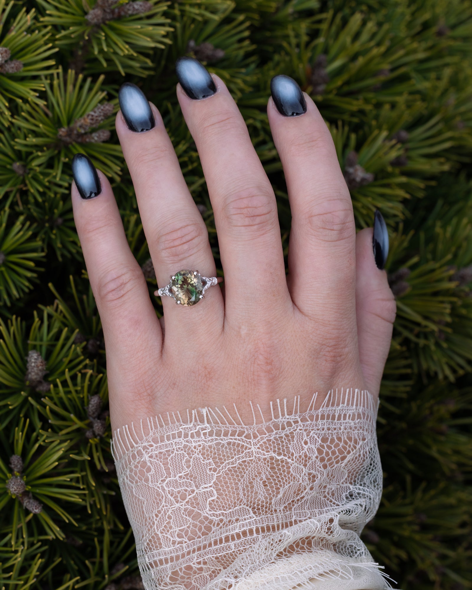 Hand with a sunstone ring on a background of green foliage