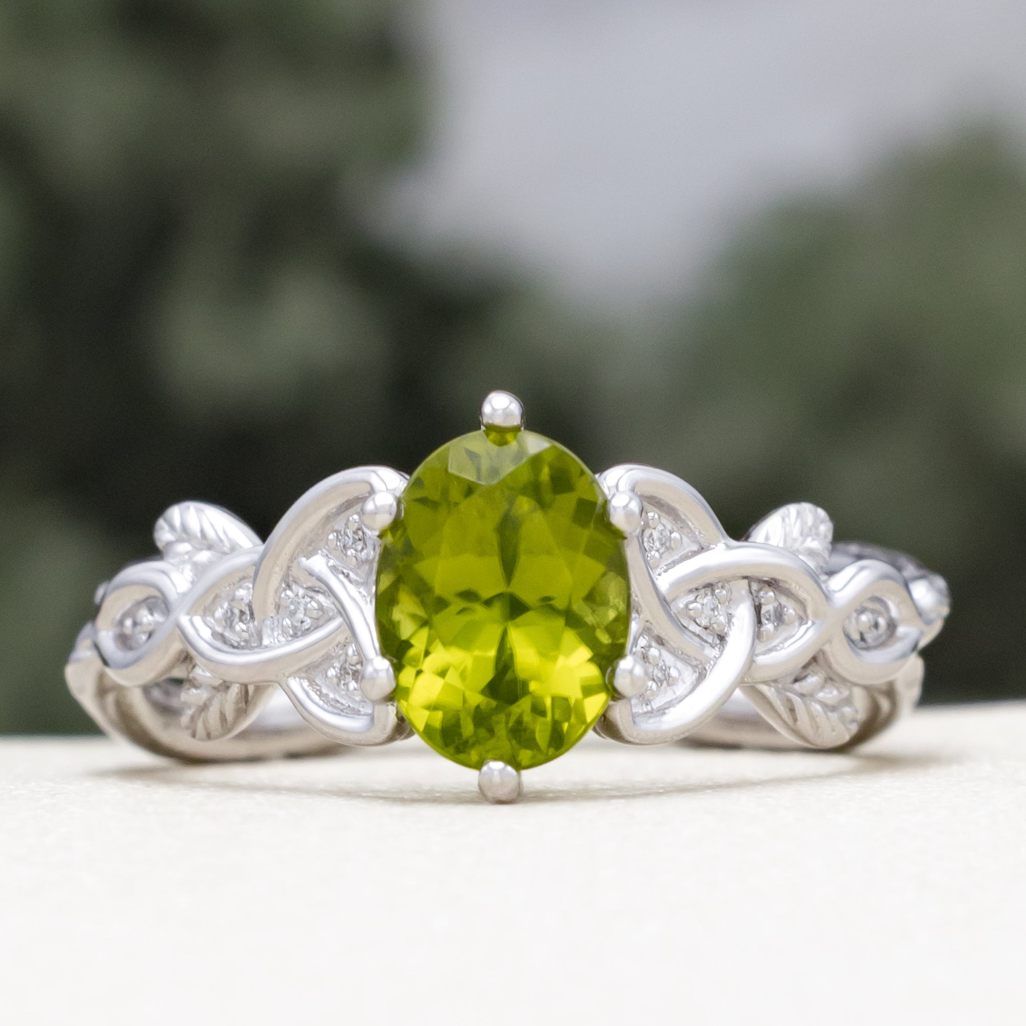 White gold ring with a green peridot on a blurred natural background