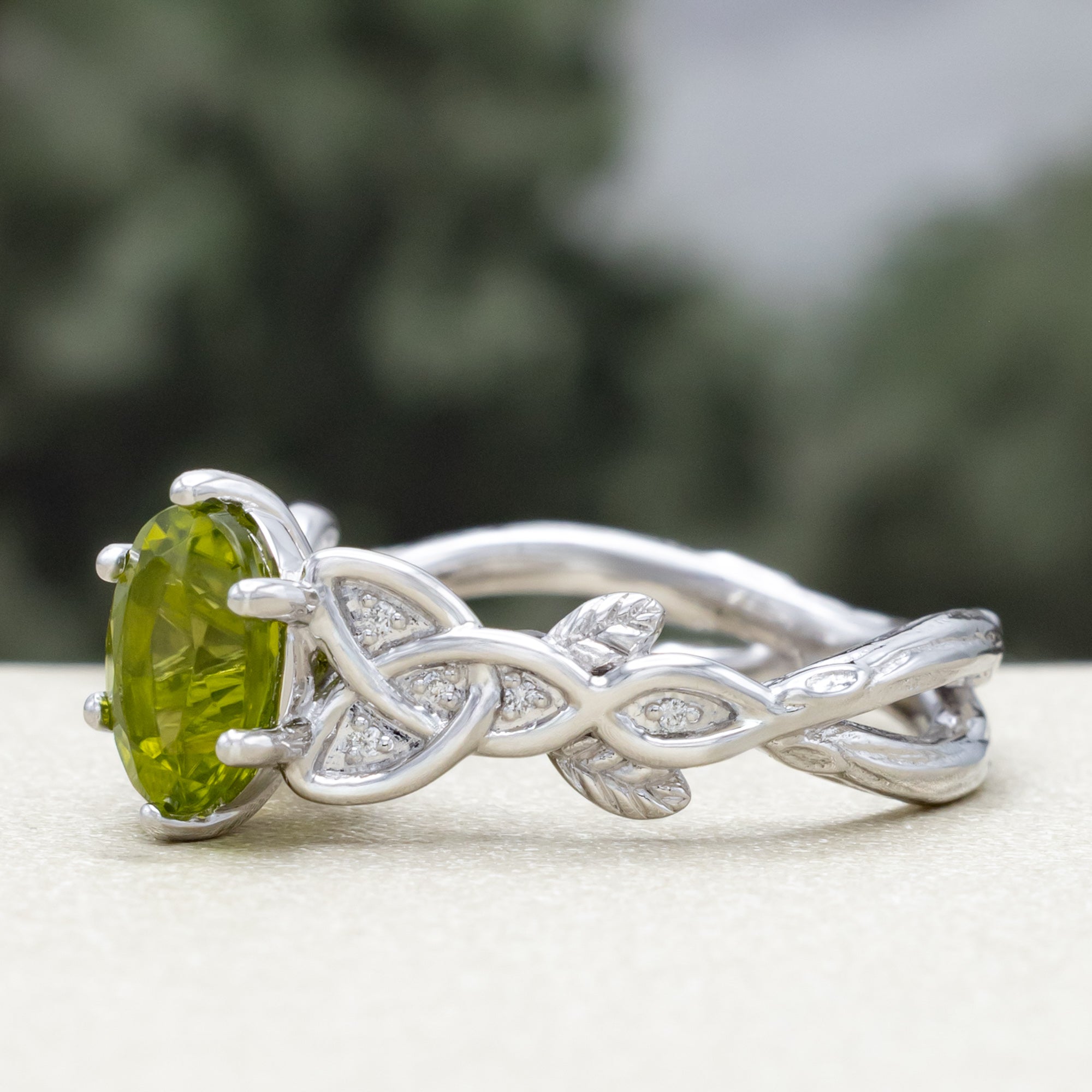 White gold ring with a green peridot on a blurred natural background